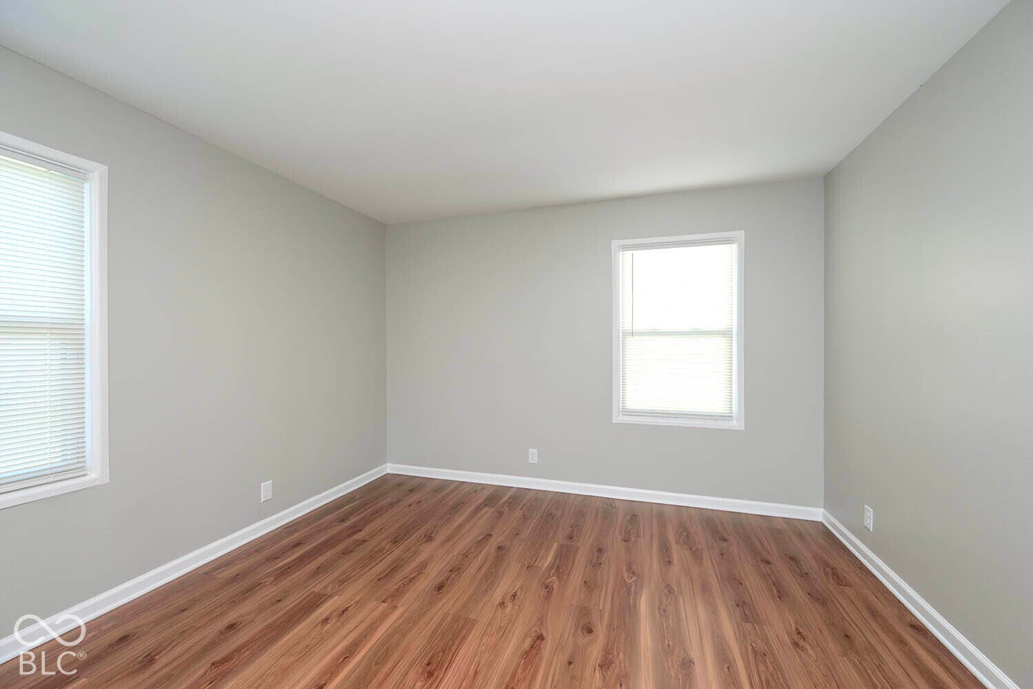 Wood-finish flooring with white trim, light gray walls, and two windows with blinds