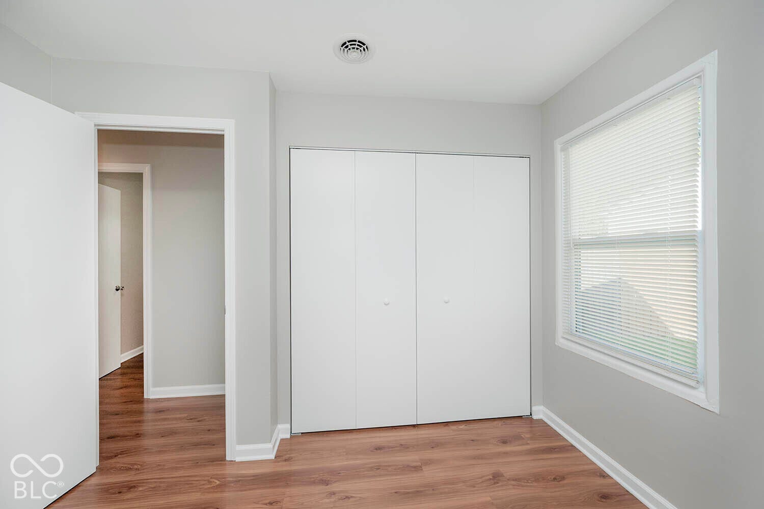 Wood-finish flooring, white bi-fold closet doors, white window blinds, white trim, and light gray wall paint