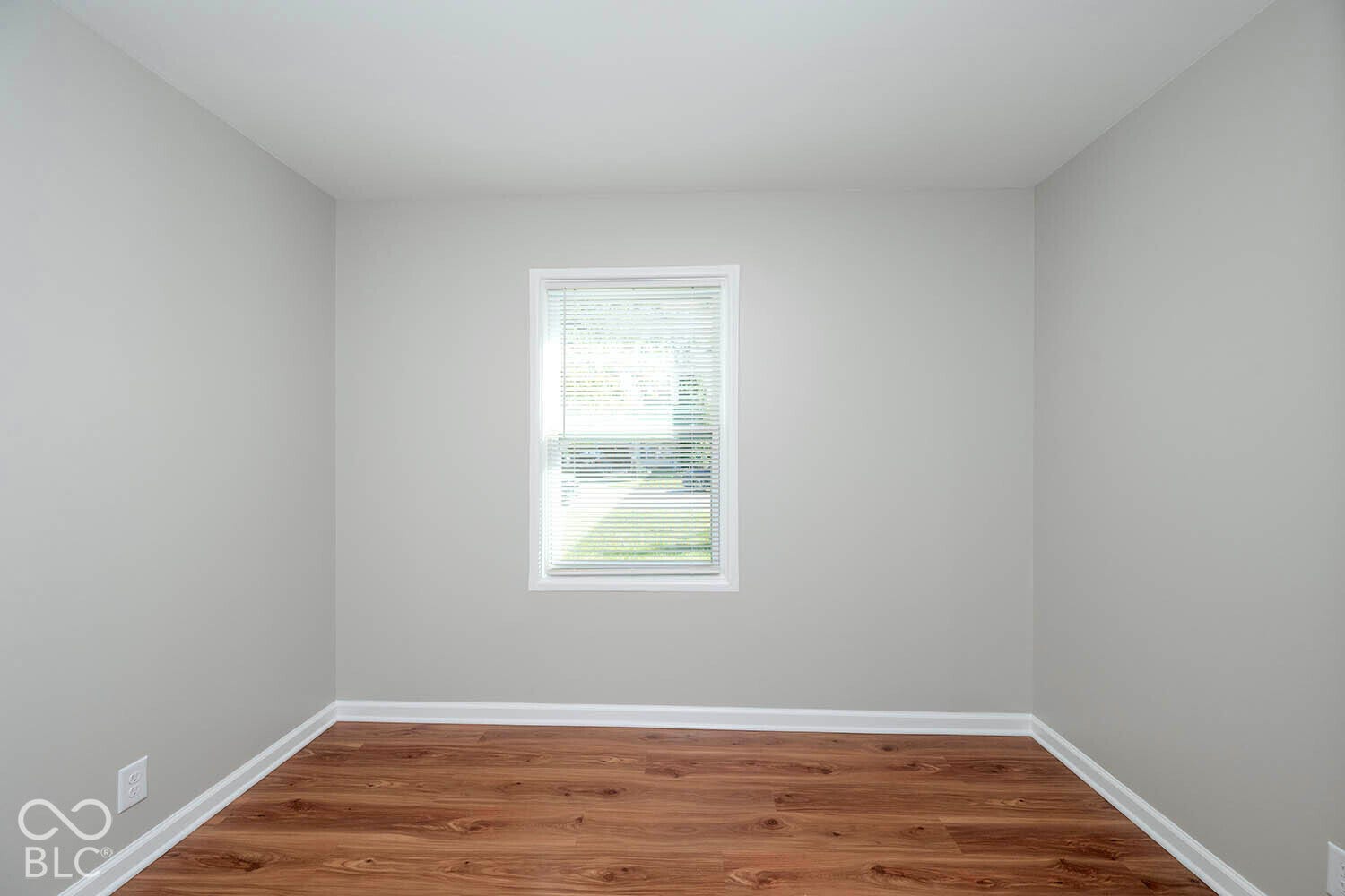 Neutral wall finish, wood-finish flooring, white trim, and a window with blinds
