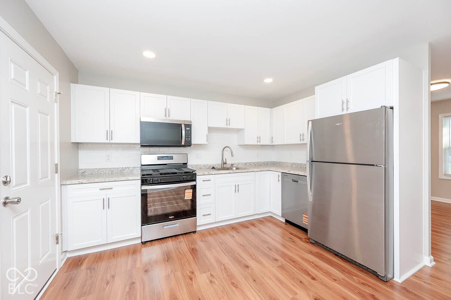 White cabinetry with brushed nickel hardware, stainless steel appliances, light-toned countertops, white subway tile backsplash, and wood-finish flooring