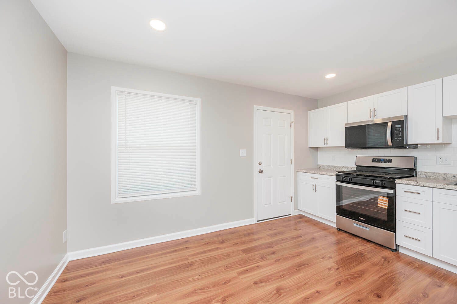 Wood-finish flooring, white cabinetry, stainless steel appliances, speckled countertops, and white subway tile backsplash