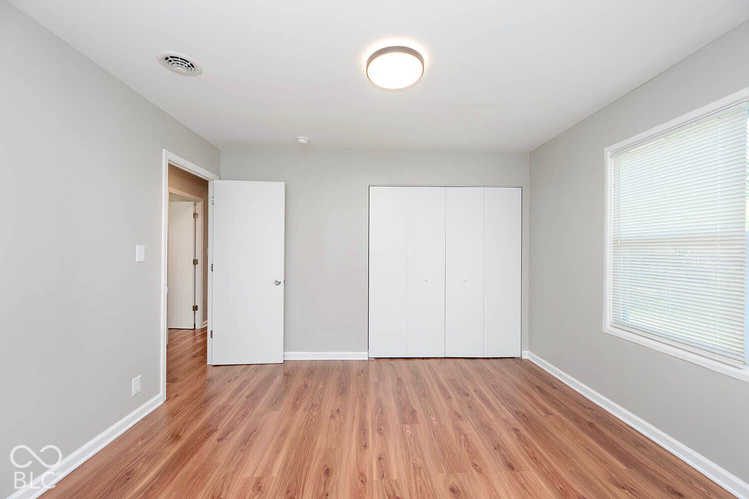 Wood-finish flooring, light gray walls, white baseboards, a flush-mount ceiling light, and a window with blinds