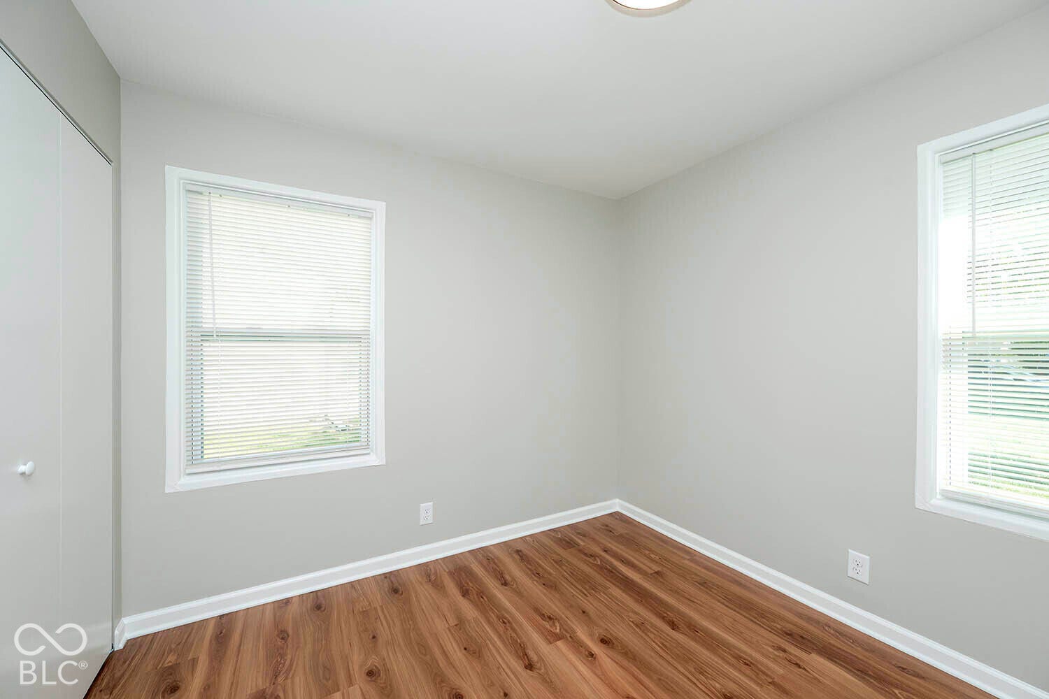 Wood-finish flooring, white trim, recessed ceiling light, two windows with white blinds, and a built-in closet with white doors