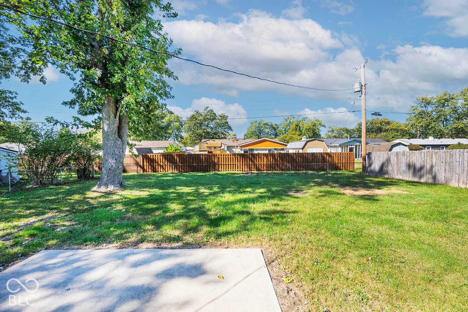 Expansive green lawn with a mature tree, bordered by wood fencing, and a concrete patio pad