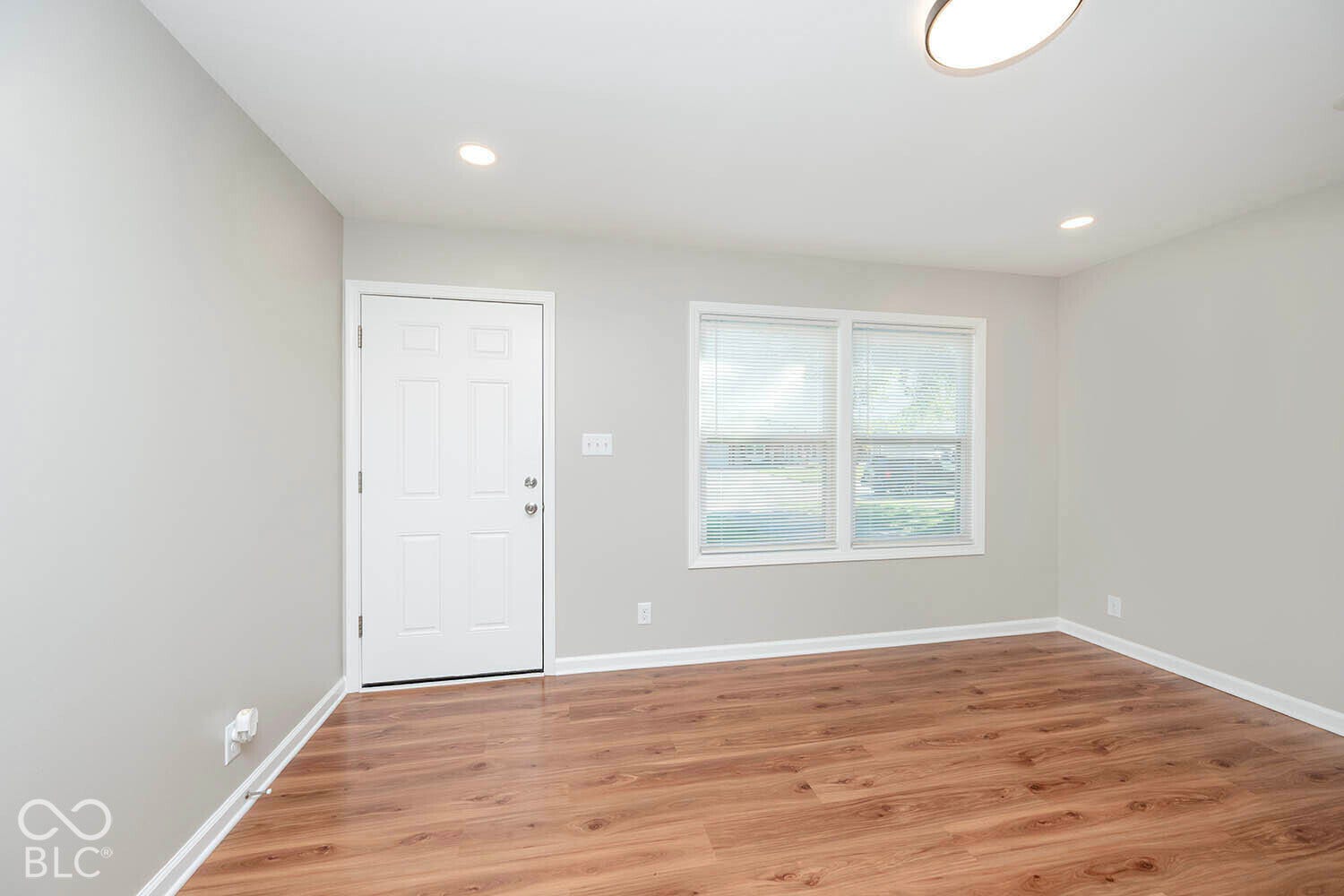 Wood-finish flooring, recessed lighting, ceiling-mounted light fixture, white interior door, and window with blinds
