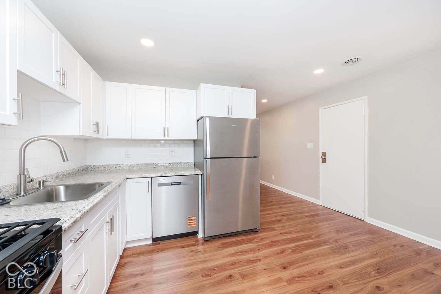 White cabinetry, stainless steel appliances, wood-finish flooring, recessed lighting, and a subway tile backsplash