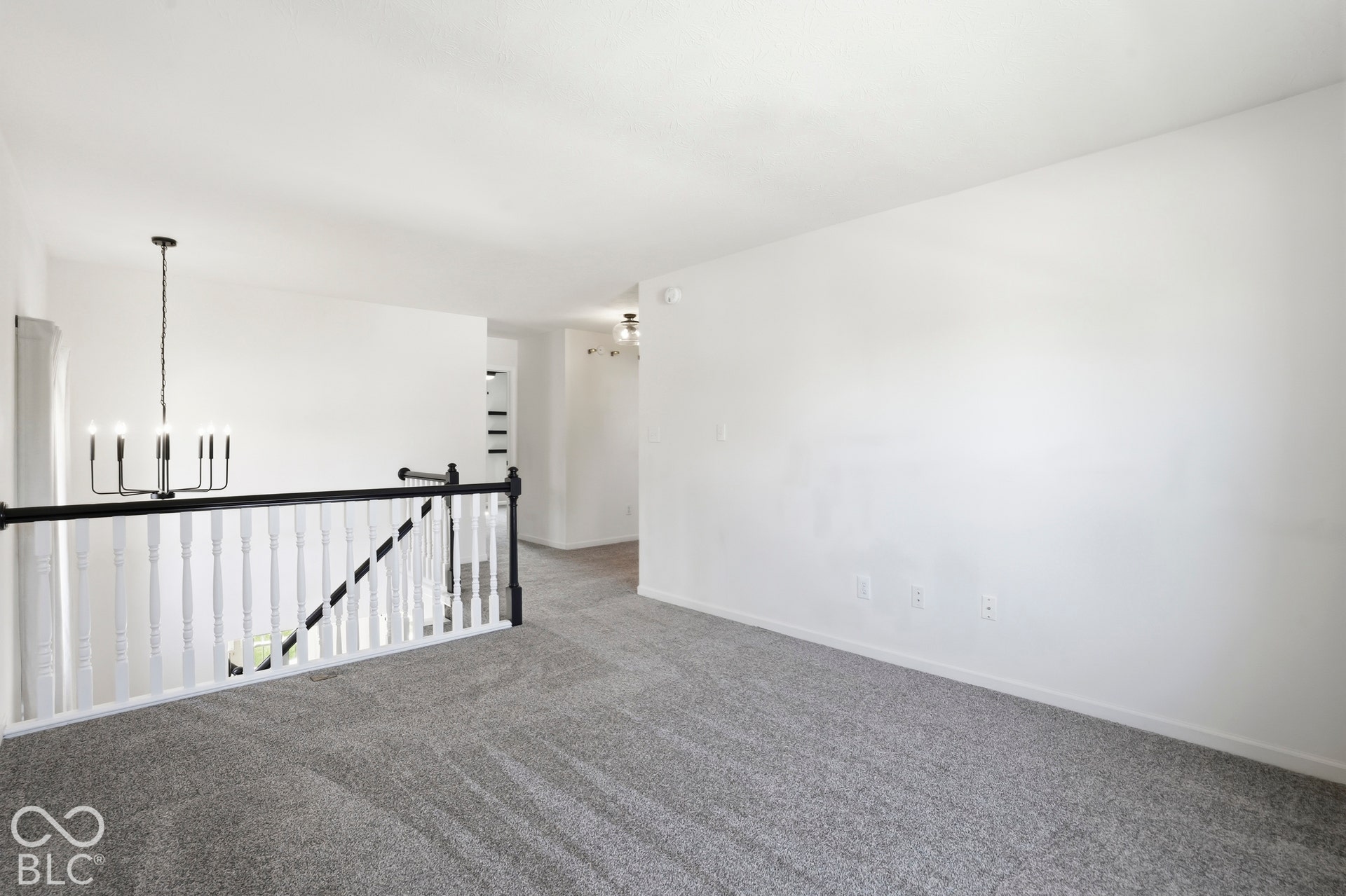 Spacious loft-style room with modern stair railing with black metal accents and white balusters.