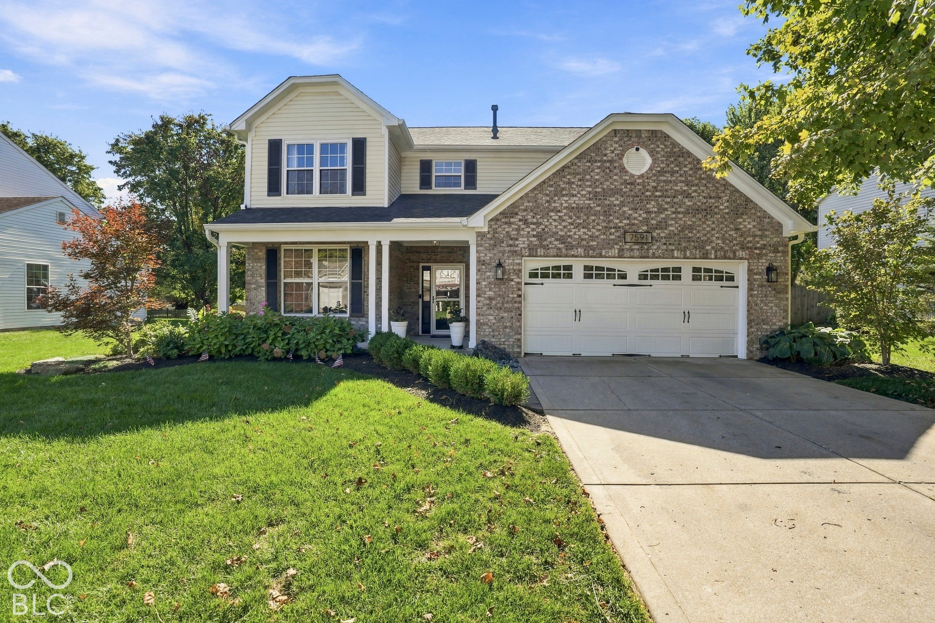 Traditional two-story residence featuring light-colored siding, a brick facade, a covered front porch with columns, a two-car garage .