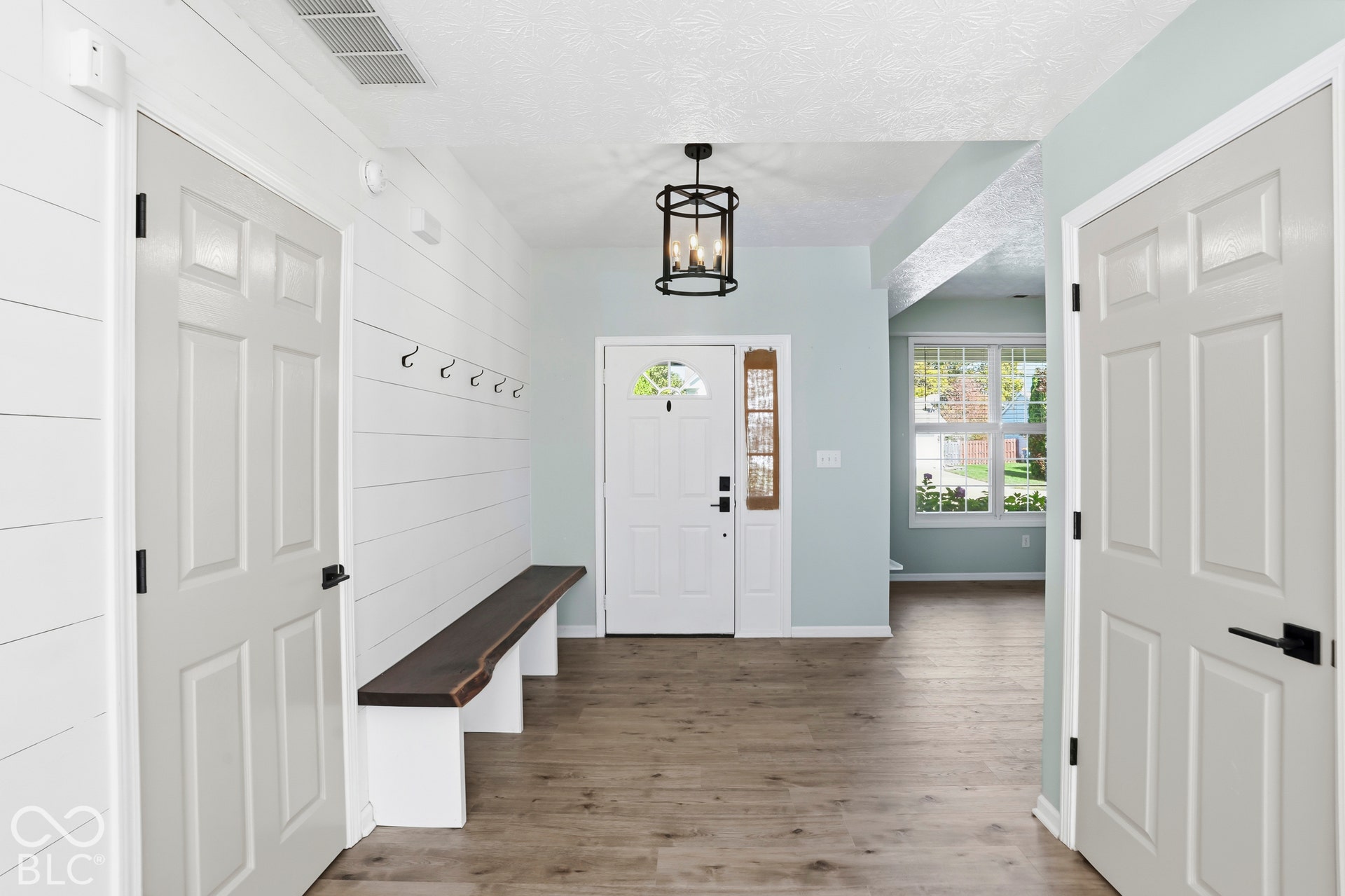 Entryway featuring wood-finish flooring, shiplap wall accent, built-in bench, and an open-cage chandelier