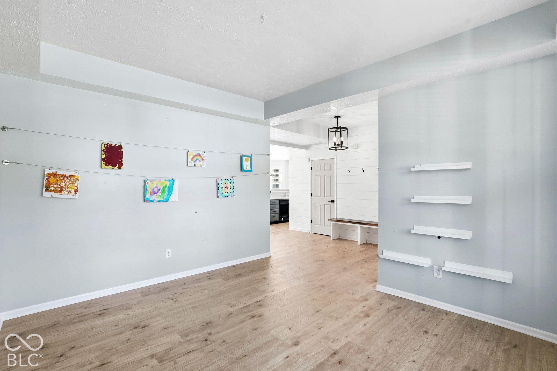 Light wood-finish flooring, light gray wall paint, built-in shelving, white trim, and a black light fixture