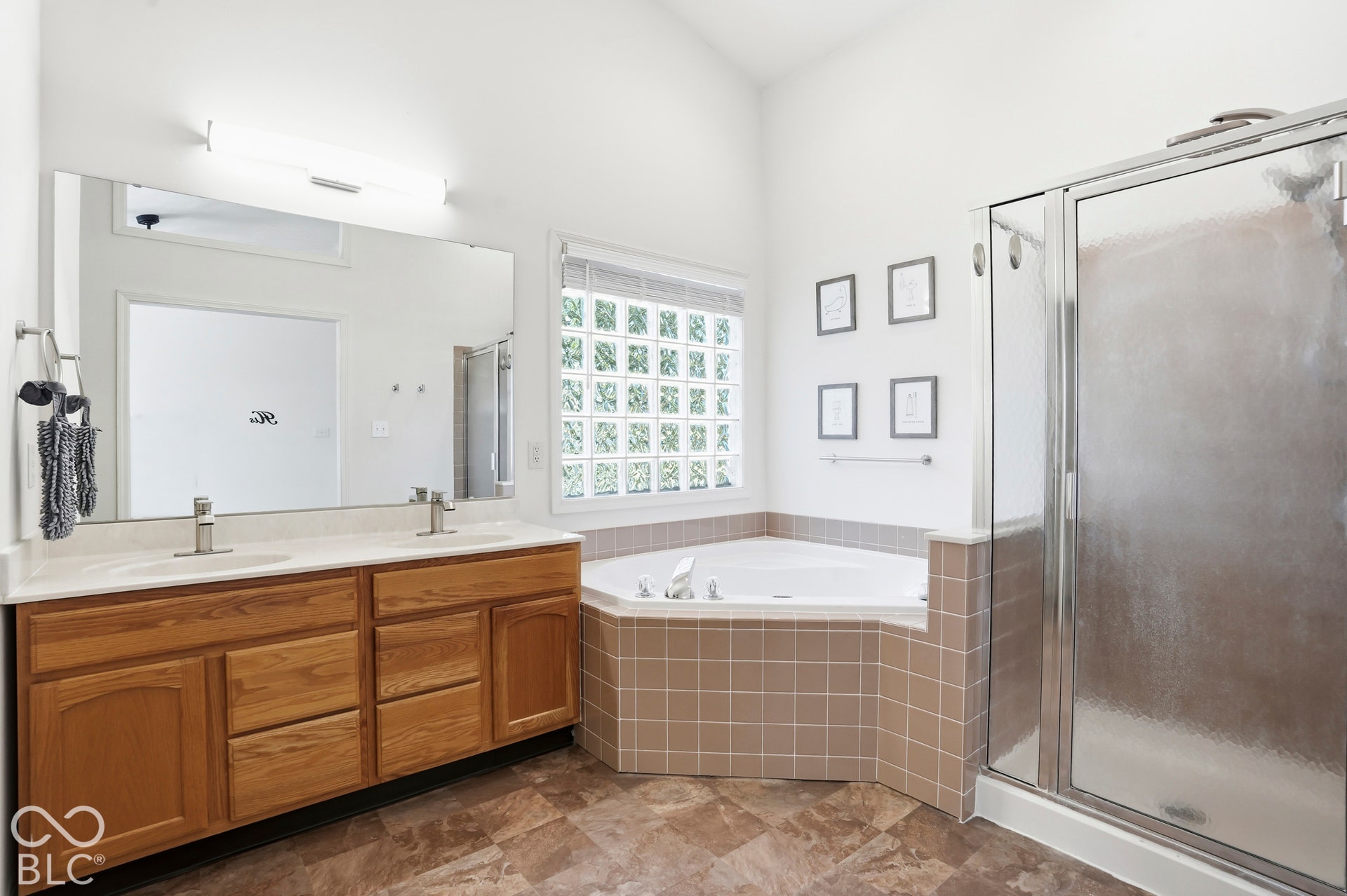 Double vanity with wood-finish cabinetry and dual sinks, tiled corner soaking tub, and enclosed shower with clear glass door
