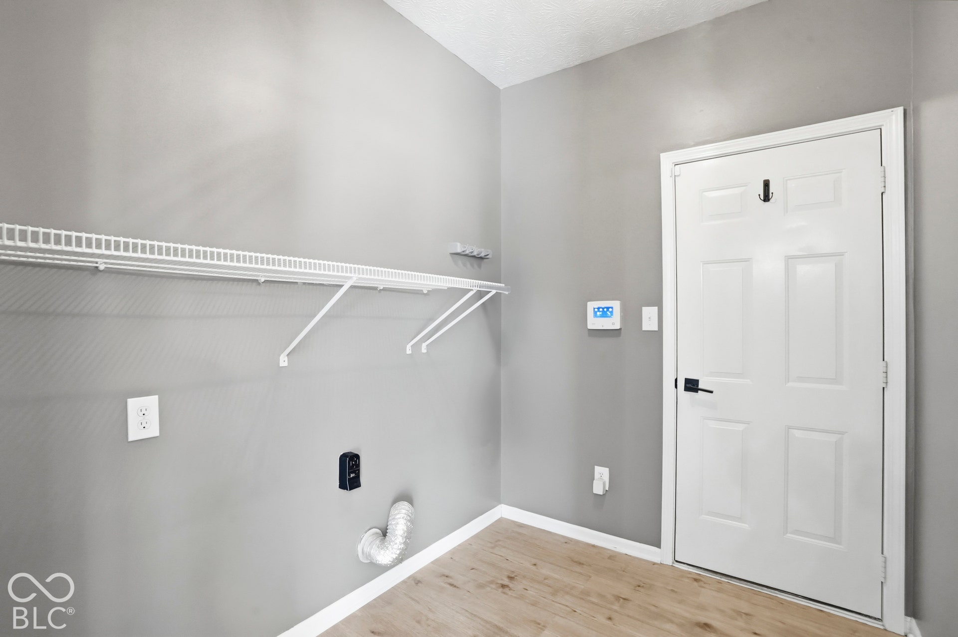 Utility space featuring wire shelving, wood-finish flooring, a white panel door with black hardware, and a digital thermostat