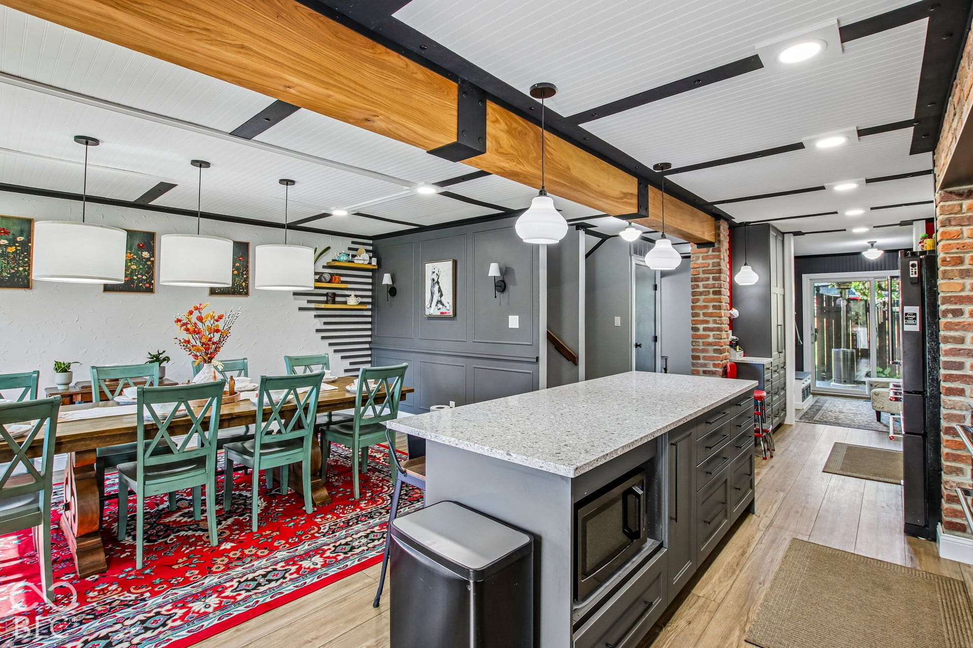 Spacious kitchen with a large island, wood-finish flooring, exposed brick accents, and a paneled ceiling with exposed beams