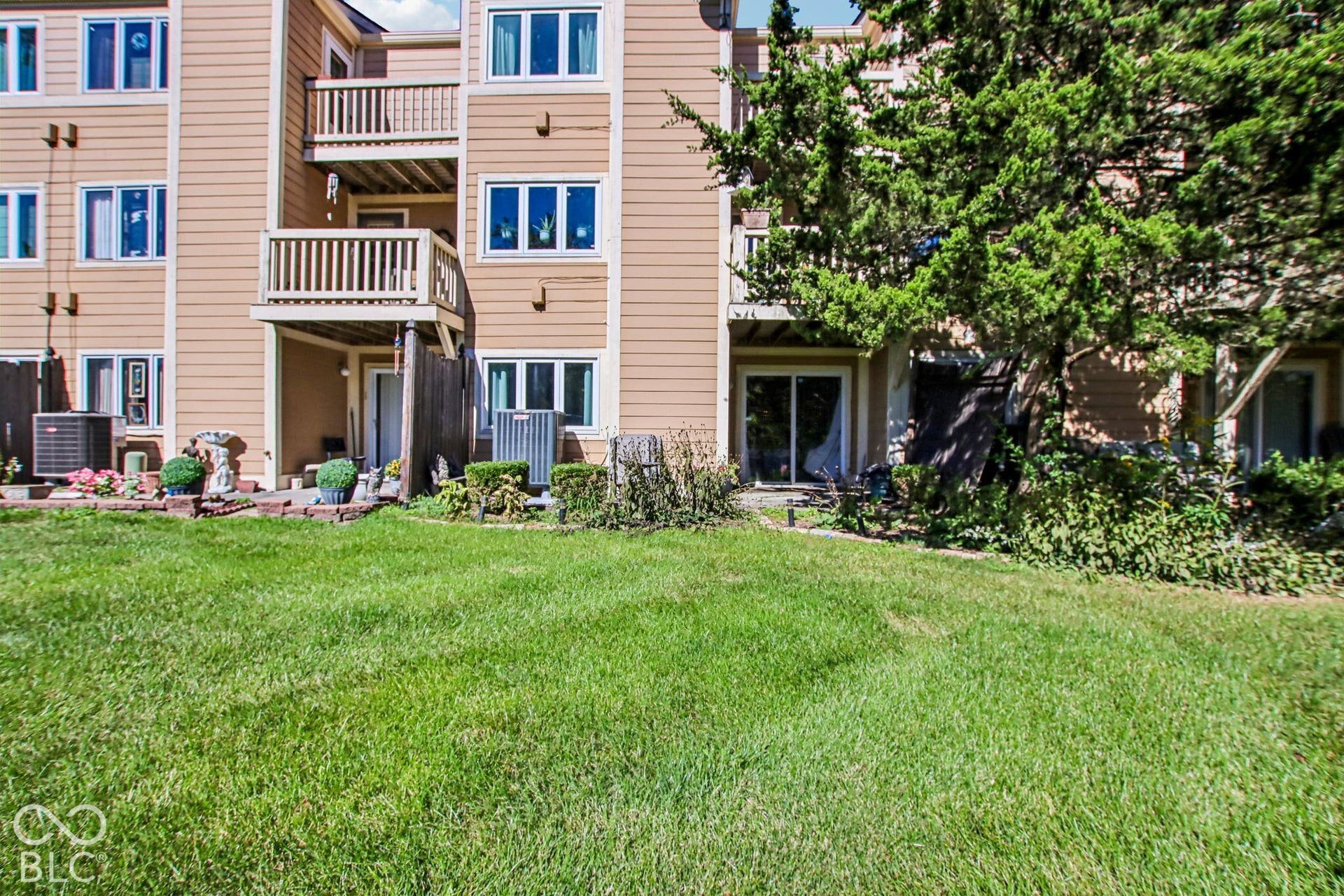 Expansive green lawn with mature landscaping, multiple balconies, and ground-level patios