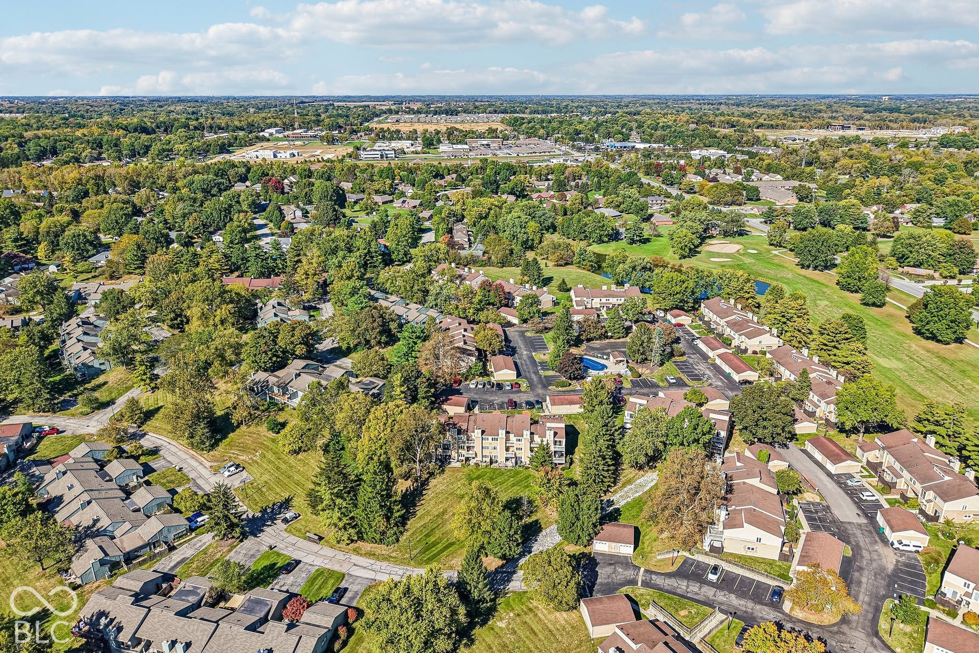 Expansive community featuring mature trees, residential structures, paved roadways, and a communal swimming pool