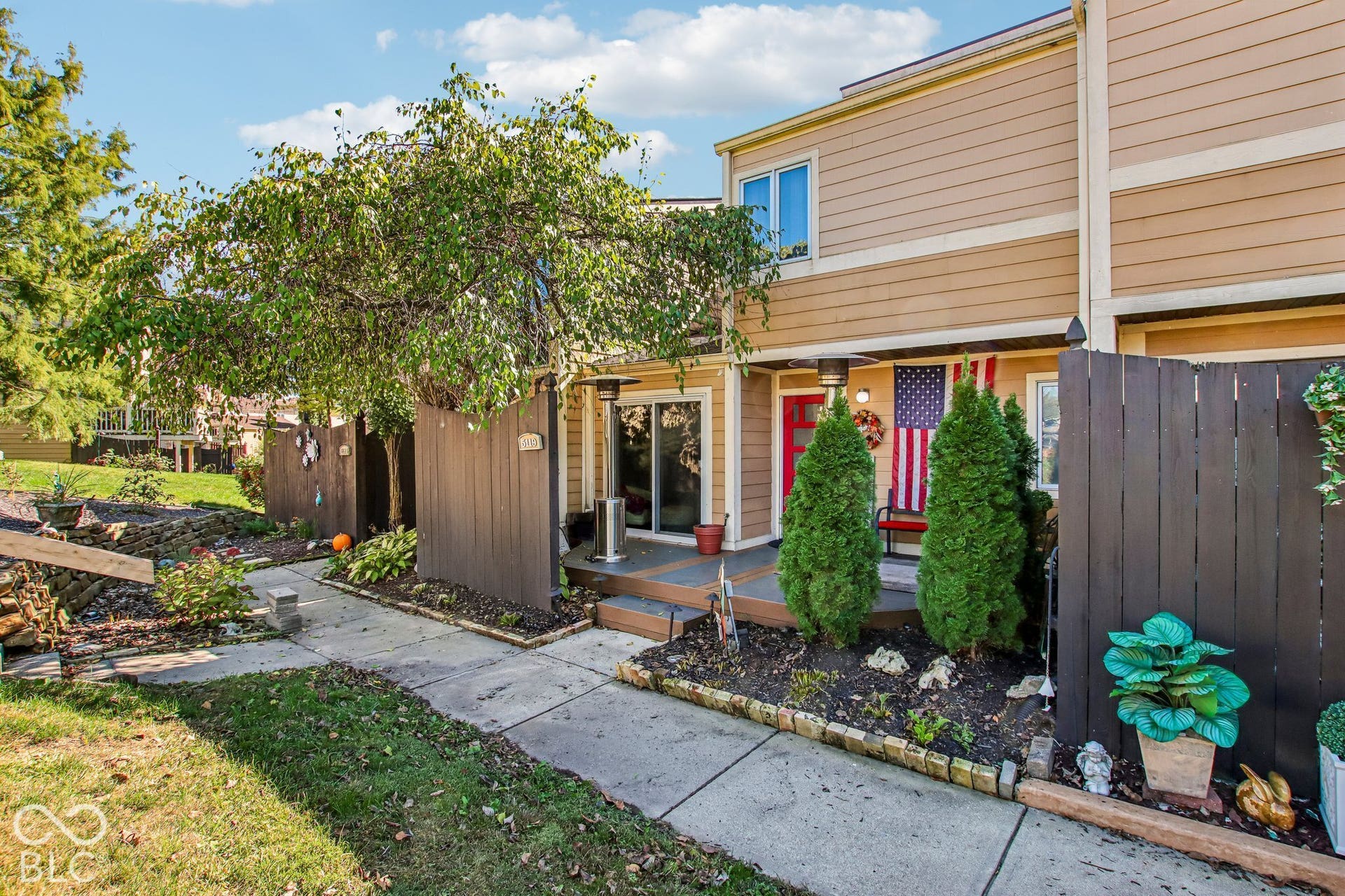 Tan siding exterior featuring a red entry door, a ground-level patio, and a privacy fence