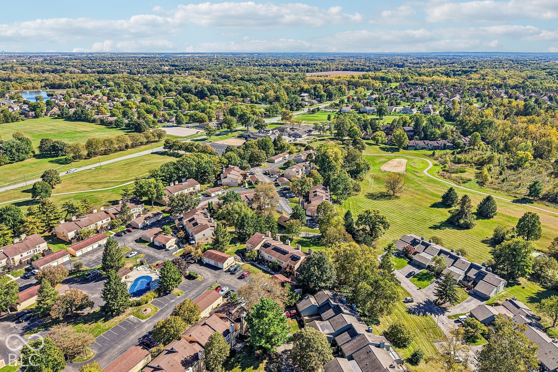 Expansive aerial perspective showcasing a residential community with mature trees, green spaces, a community pool, and a nearby golf course