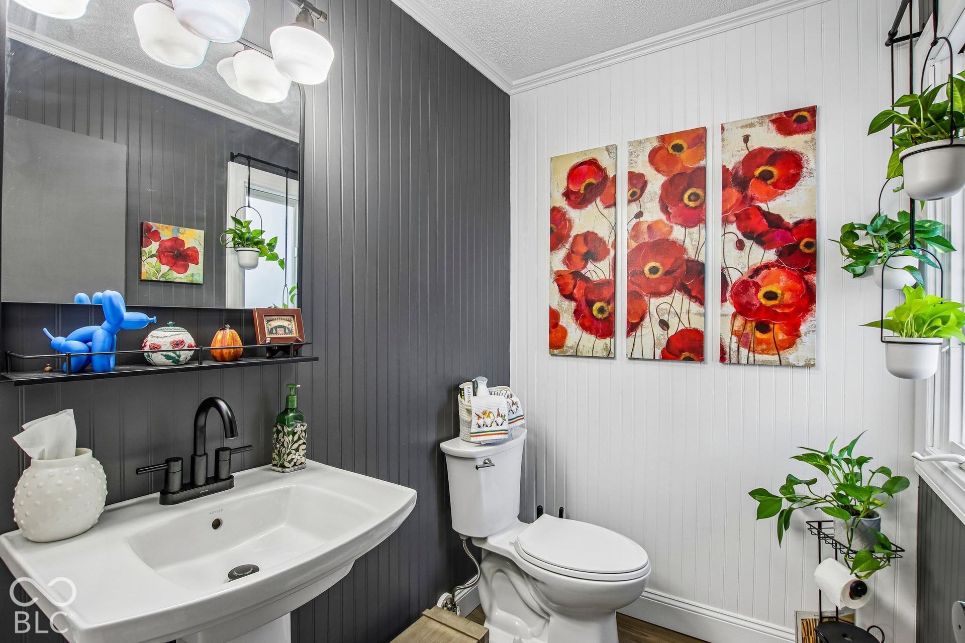 Pedestal sink with a matte black faucet, wall-mounted mirror, and beadboard paneling