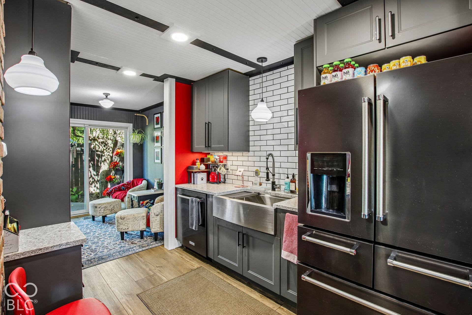 Modern kitchen featuring dark gray cabinetry, stainless steel farmhouse sink, white subway tile backsplash, and light wood-finish flooring