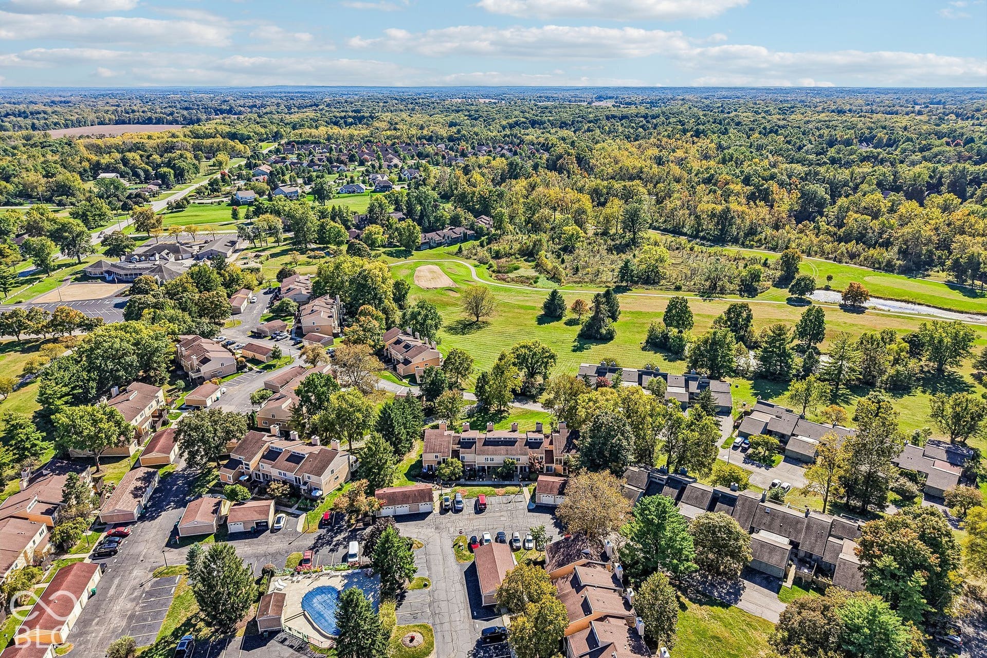 Residential community featuring multiple buildings, expansive green spaces, mature trees, and a golf course