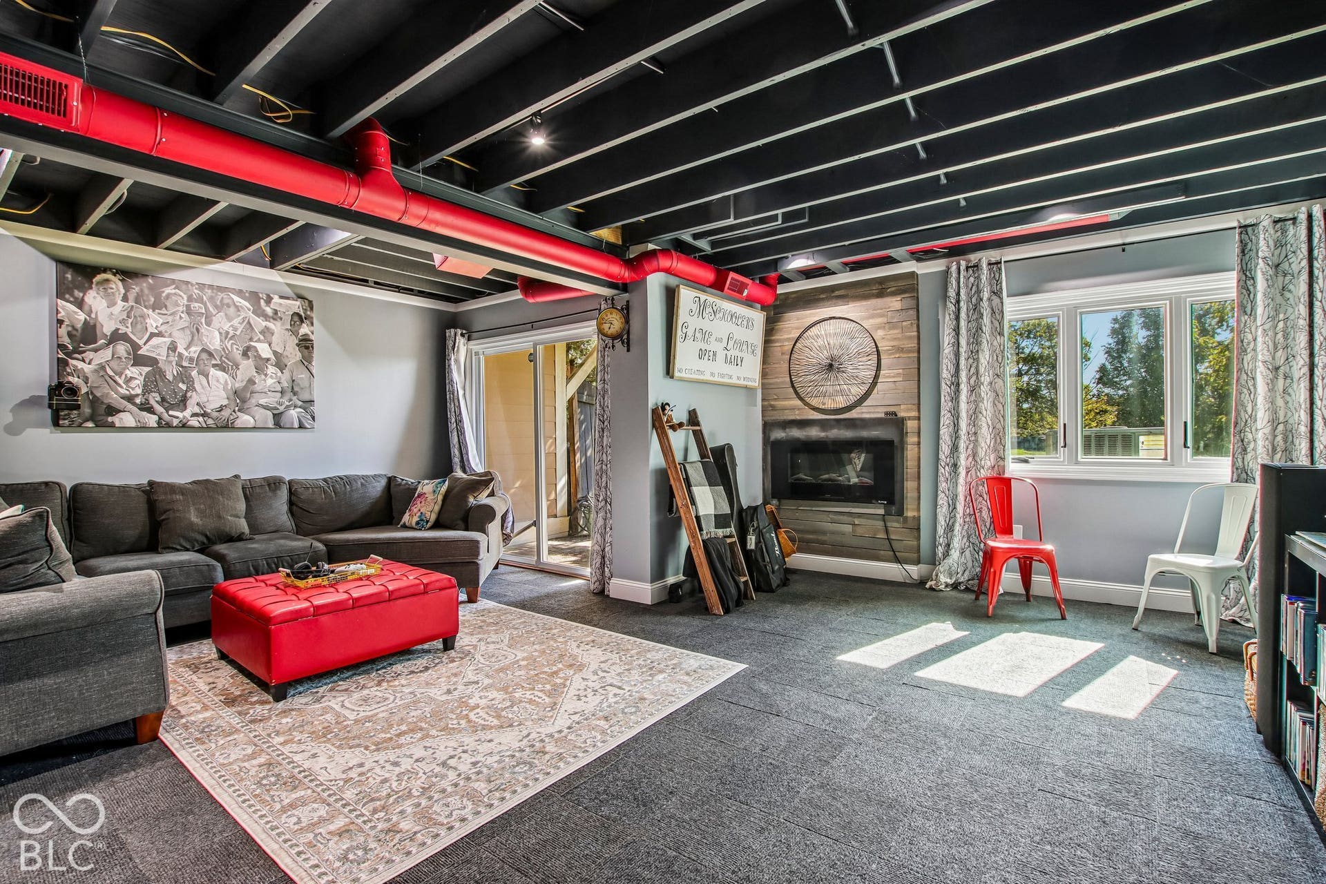 Exposed ceiling beams with red piping, recessed lighting, built-in fireplace with wood-finish paneling, multiple windows, and walk-out access