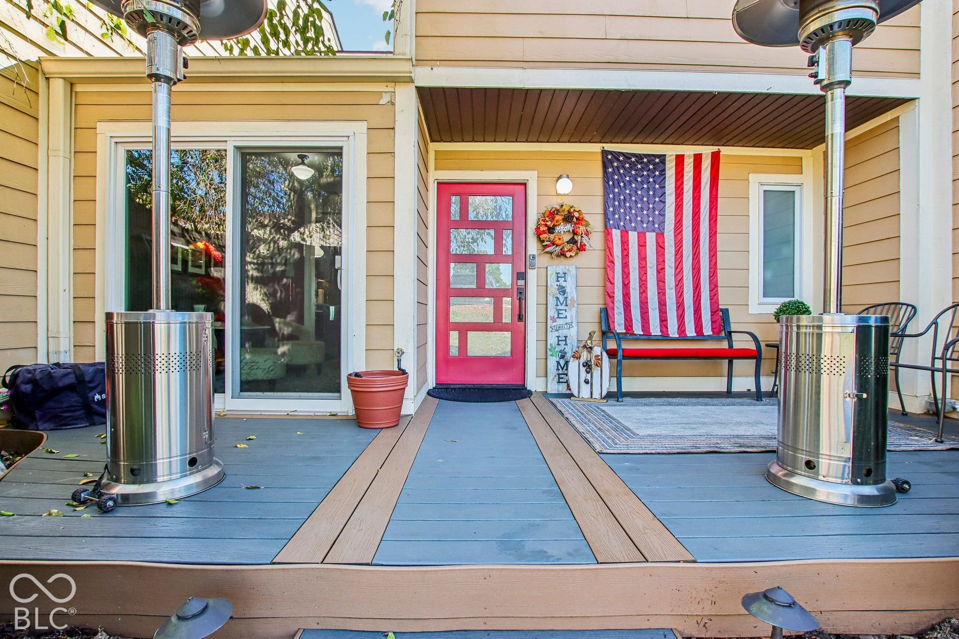 Front entry deck featuring multi-toned composite decking, a red entry door with glass inserts, and tan siding