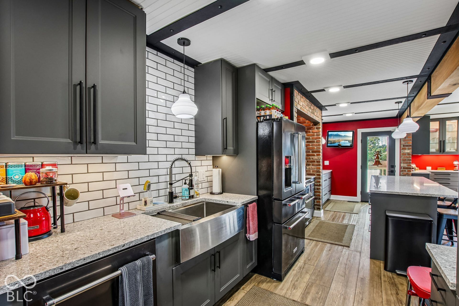 Kitchen featuring dark cabinetry, subway tile backsplash, stainless steel farmhouse sink, and wood-finish flooring