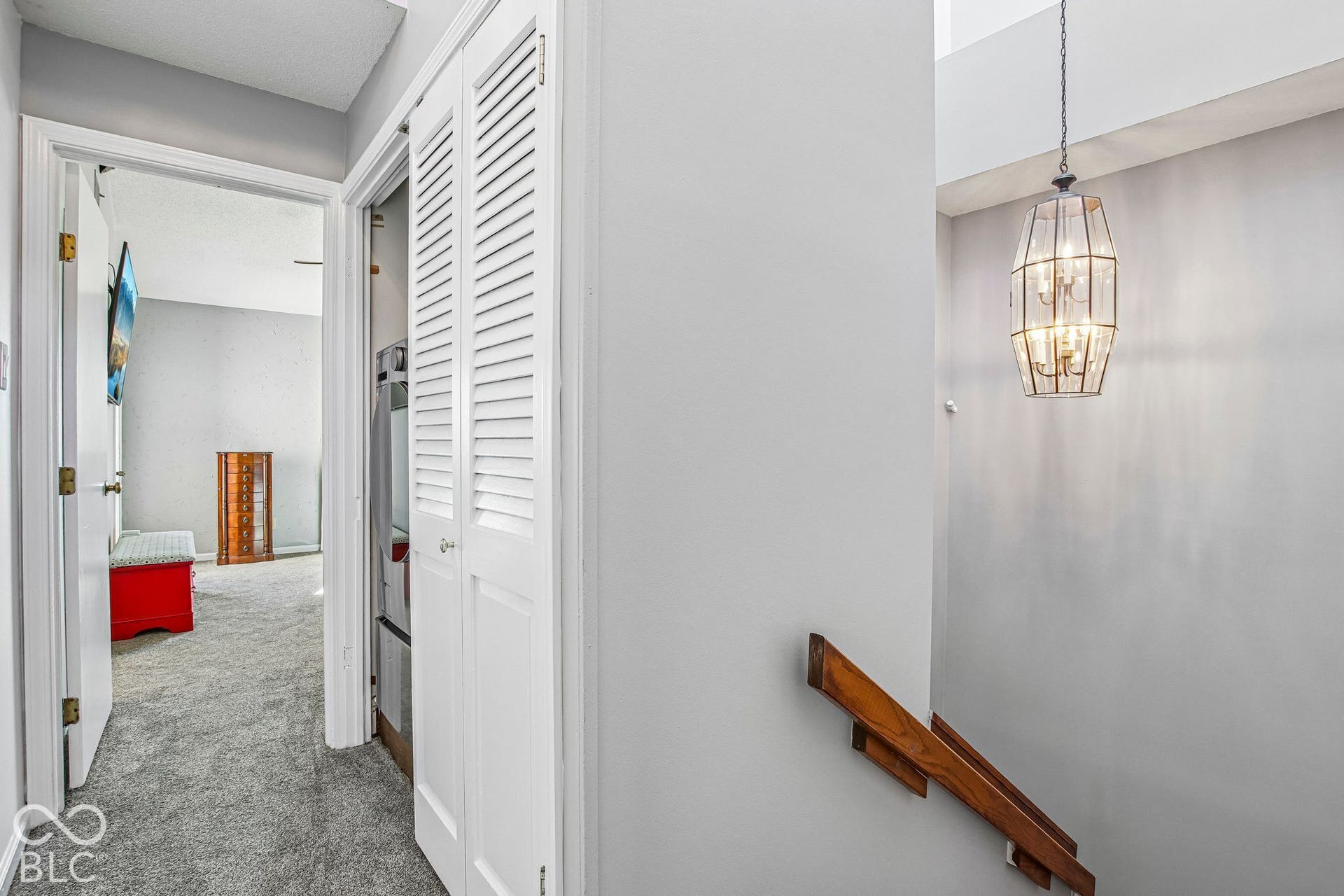 Contemporary chandelier with glass panels, wood-finish handrail, and louvered closet doors