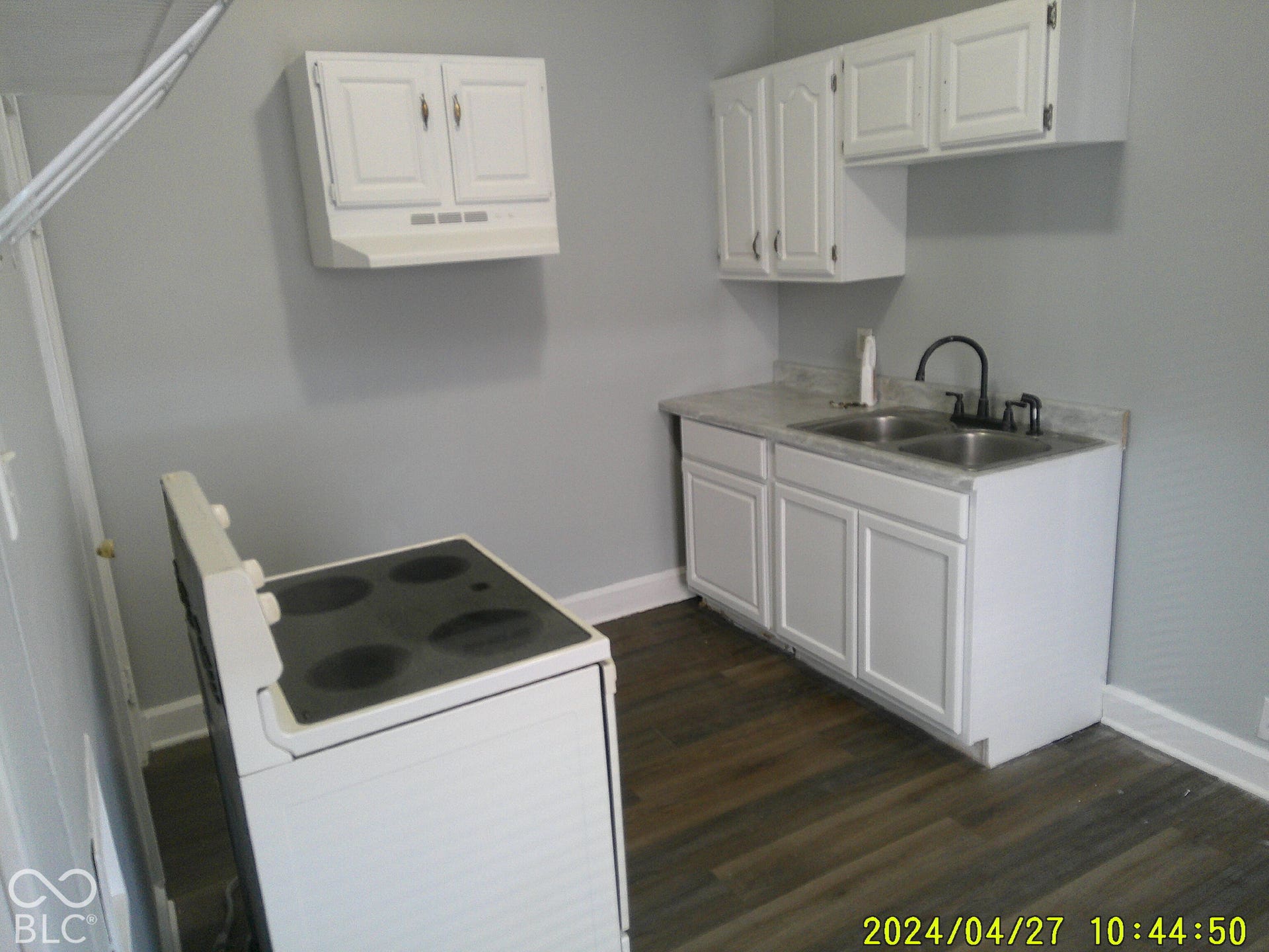 White cabinetry, dual basin stainless steel sink, black gooseneck faucet, light-toned countertops, and wood-finish flooring