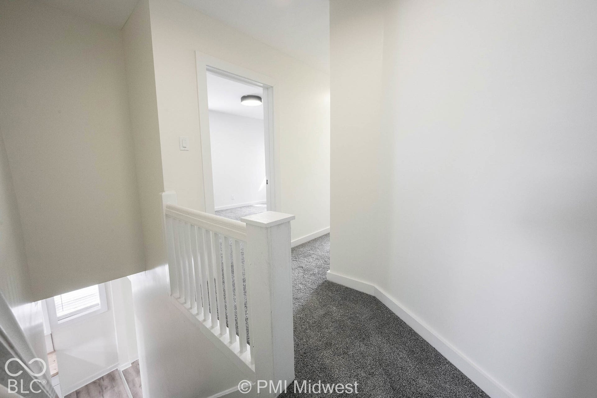 White painted baluster railing with a square newel post, gray carpet flooring, and white trim