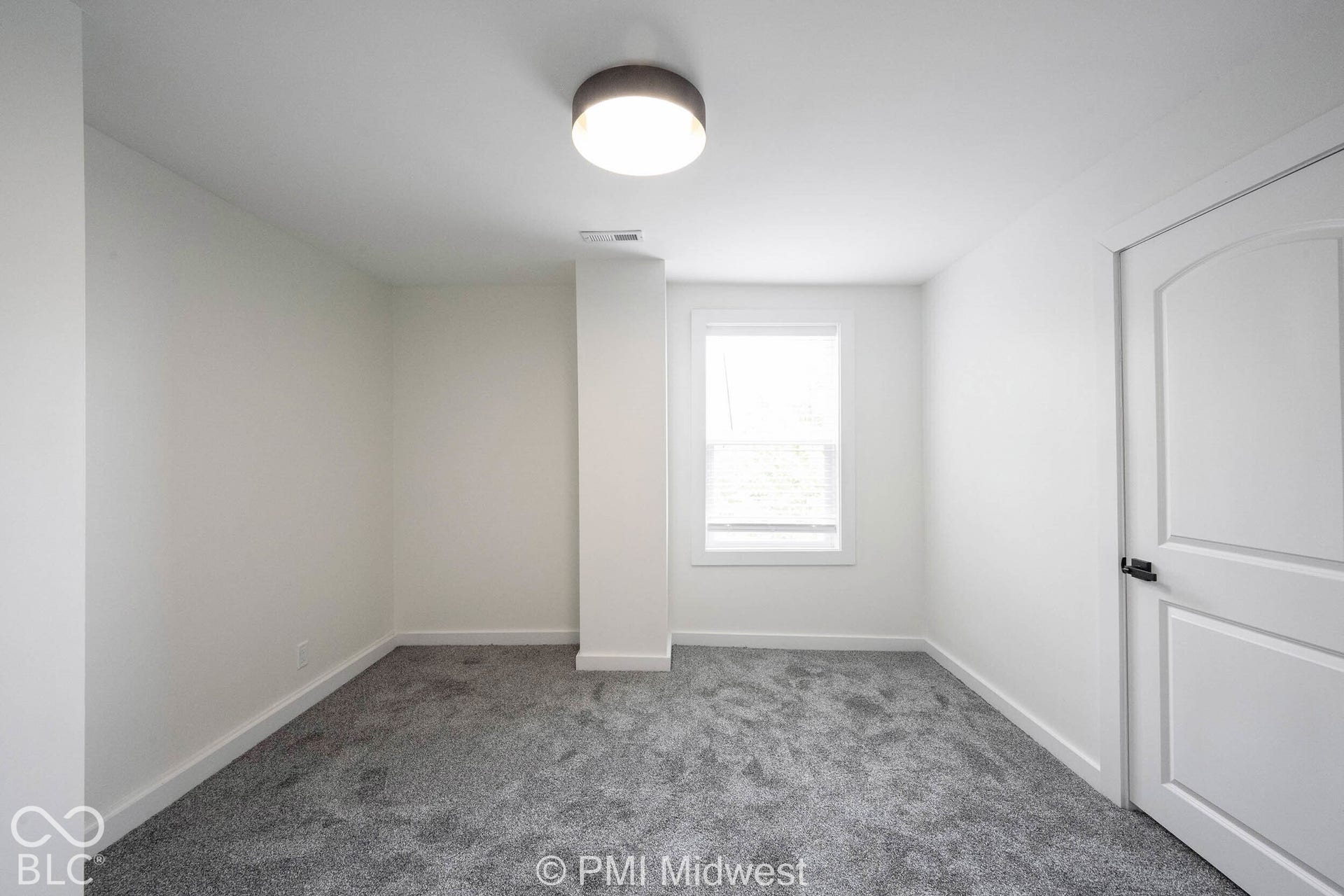 Recessed window, white trim, white paneled door with dark hardware, gray carpeted flooring, and a flush-mount ceiling light fixture