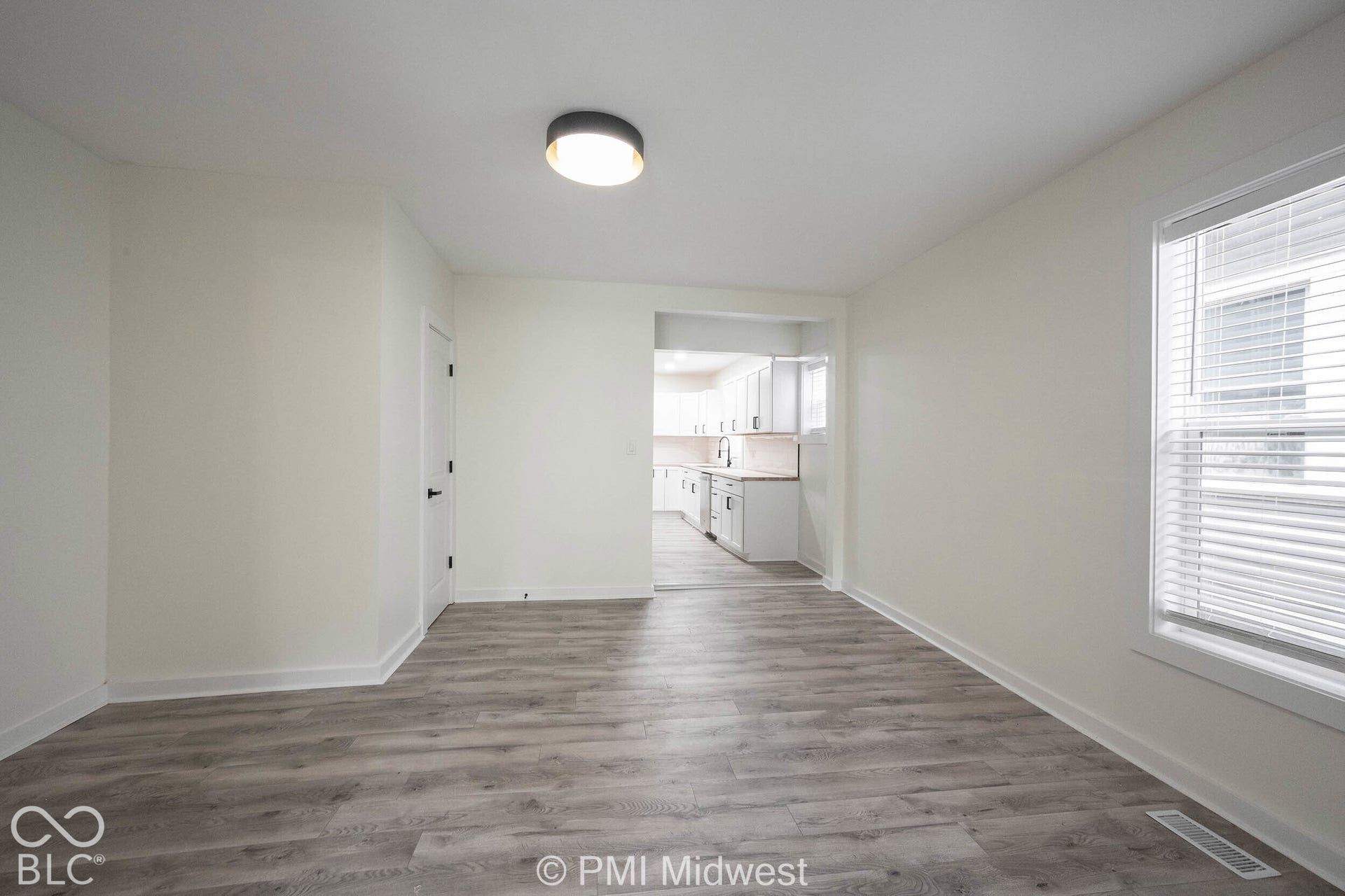 Wood-finish flooring throughout, white walls, and a recessed window with blinds