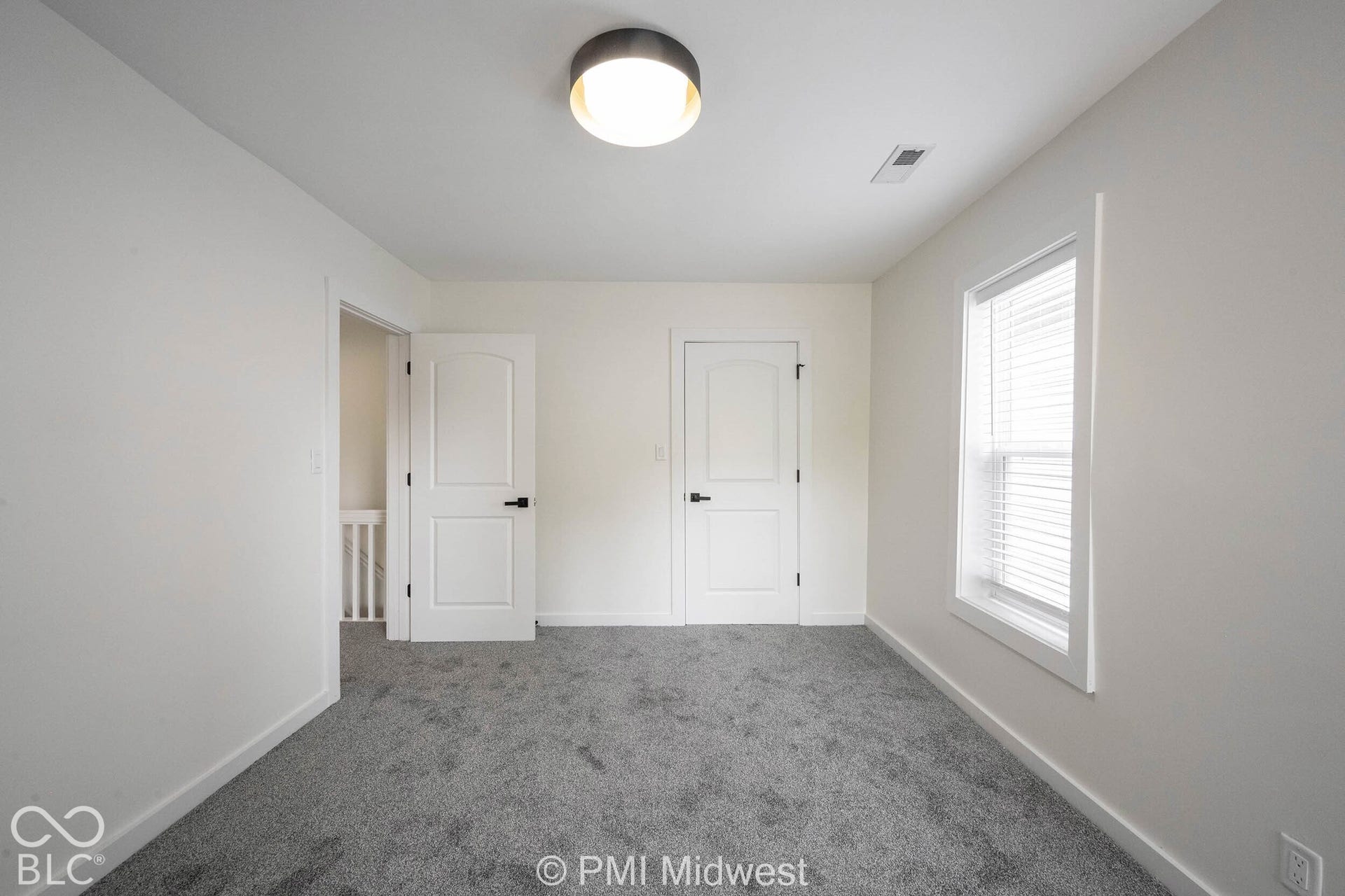 Neutral-toned wall paint, plush carpeting, white interior doors, and a window with blinds