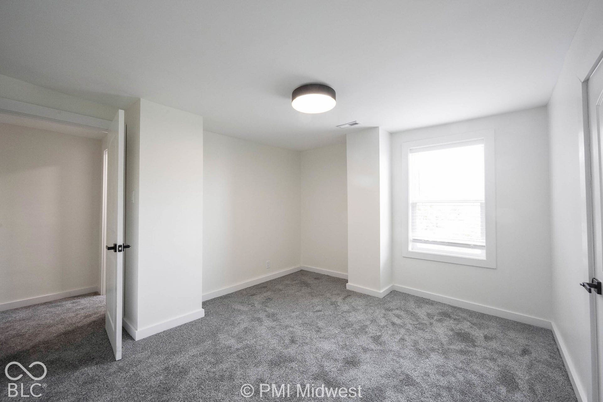 Spacious room featuring neutral paint, gray carpeting, a single window, and a flush-mount ceiling light