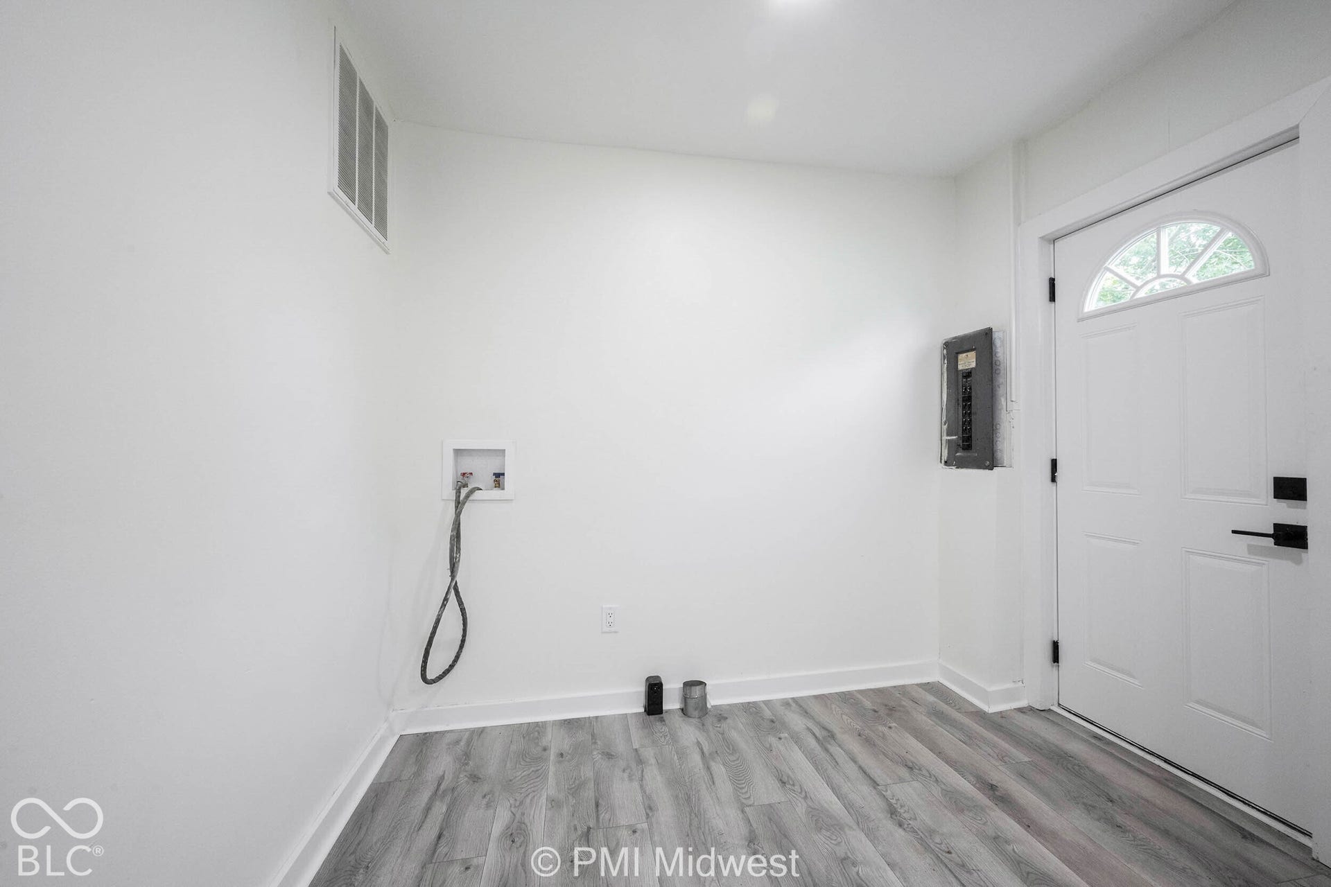 Wood-finish flooring with white trim and a white paneled door featuring an arched window