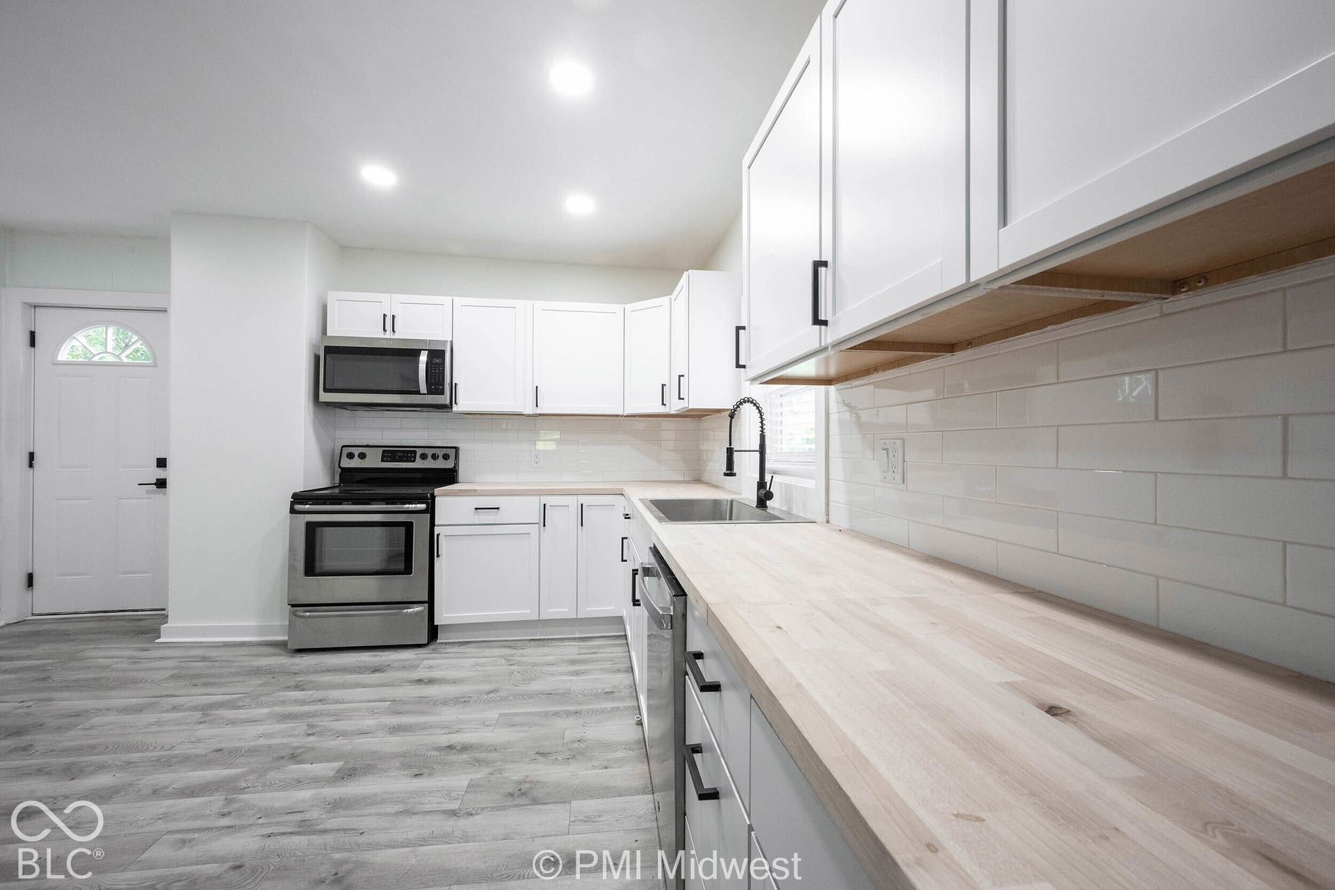 Modern kitchen featuring white shaker cabinetry, wood-finish countertops, stainless steel appliances, a subway tile backsplash, and recessed lighting
