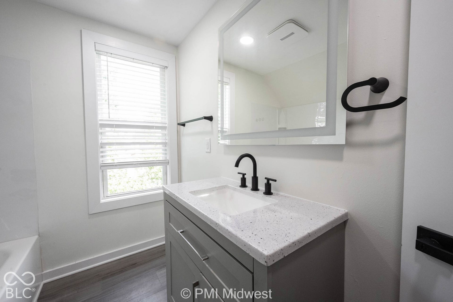 Vanity with integrated sink, black hardware, window, and wood-finish flooring