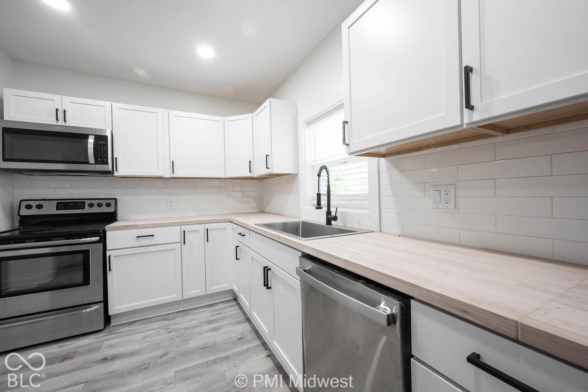 White shaker-style cabinetry with black hardware, wood-finish countertops, stainless steel appliances, white subway tile backsplash, and wood-finish flooring