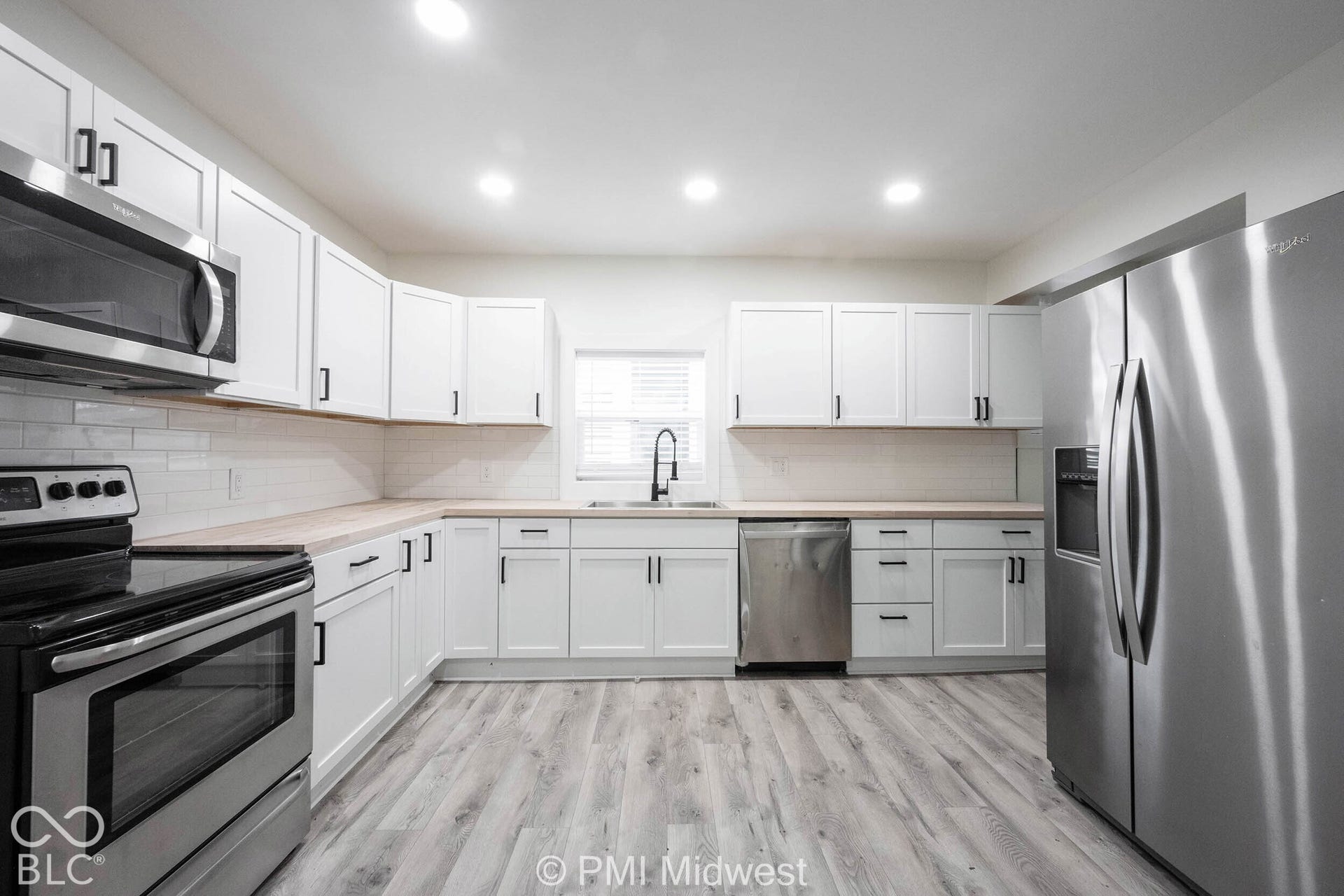 Kitchen featuring white shaker cabinetry, stainless steel appliances, wood-finish countertops, white subway tile backsplash, and wood-finish flooring