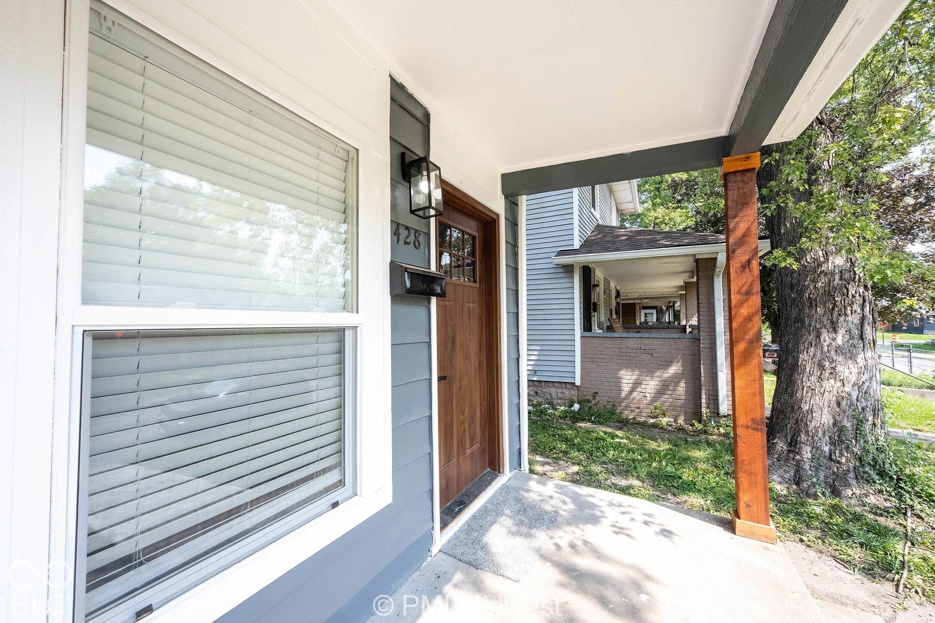 Covered front porch featuring a wood-finish support beam, wood-panel entry door, and exterior wall lantern