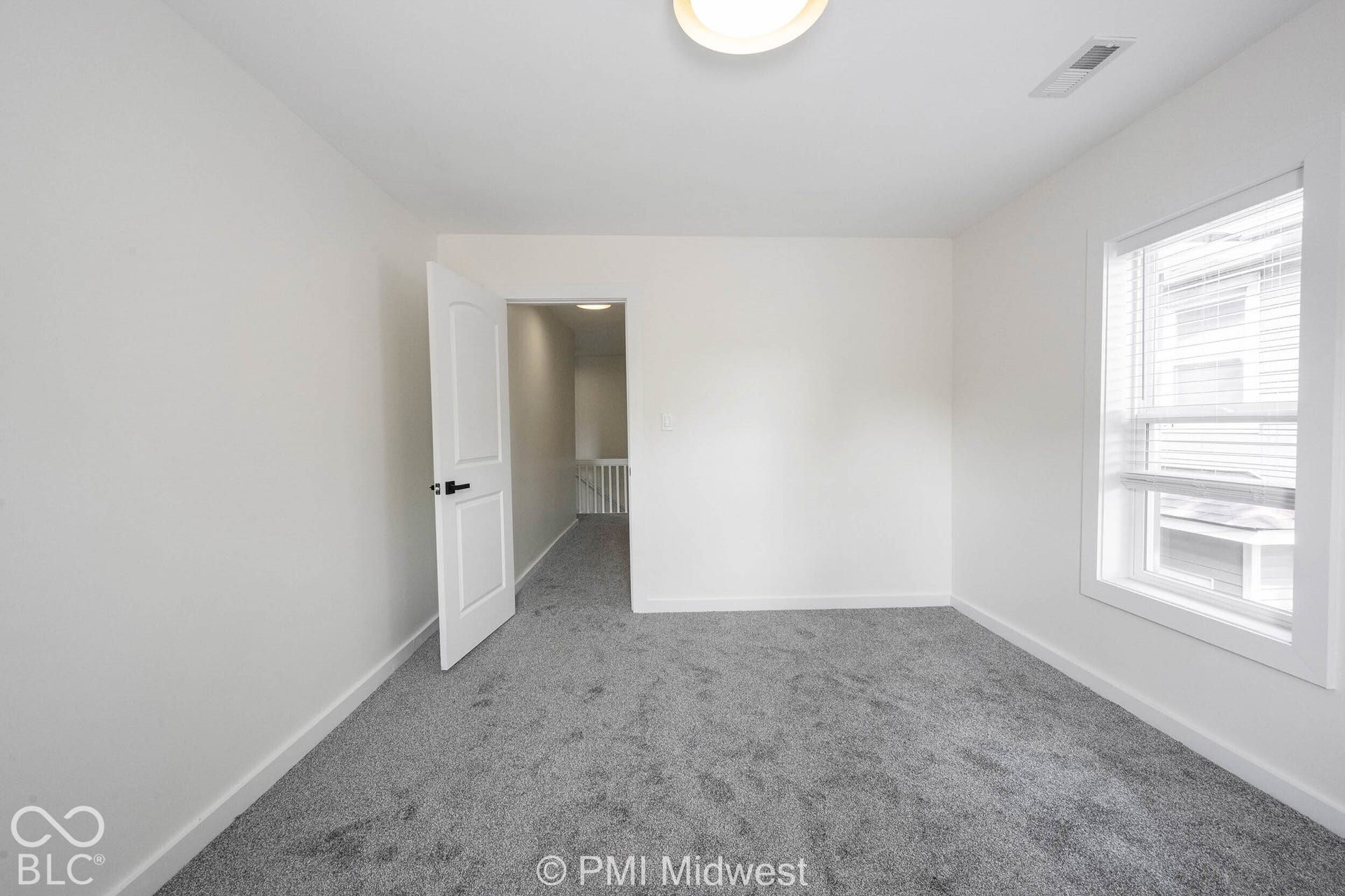 White walls with gray carpeting, an interior door with black hardware, and a window with blinds