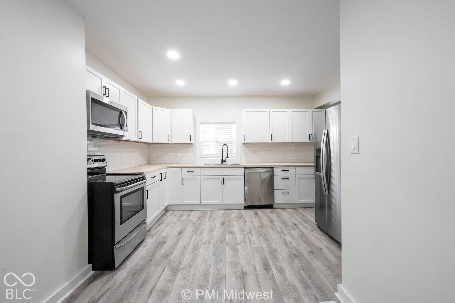 Kitchen featuring white cabinetry, light wood-finish countertops, stainless steel appliances, and wood-finish flooring