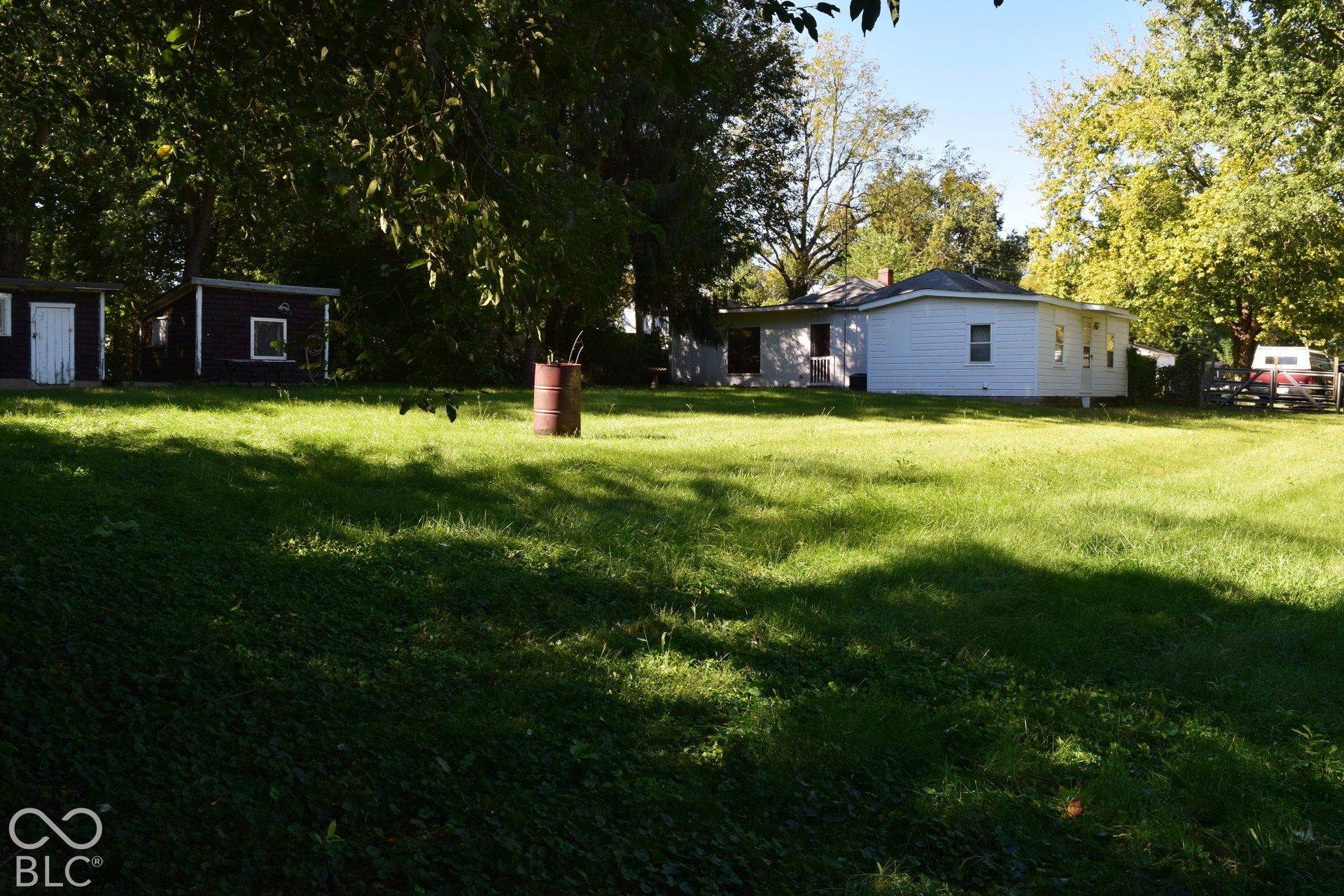 Expansive green lawn with mature persimmon tree and a detached white-sided dwelling