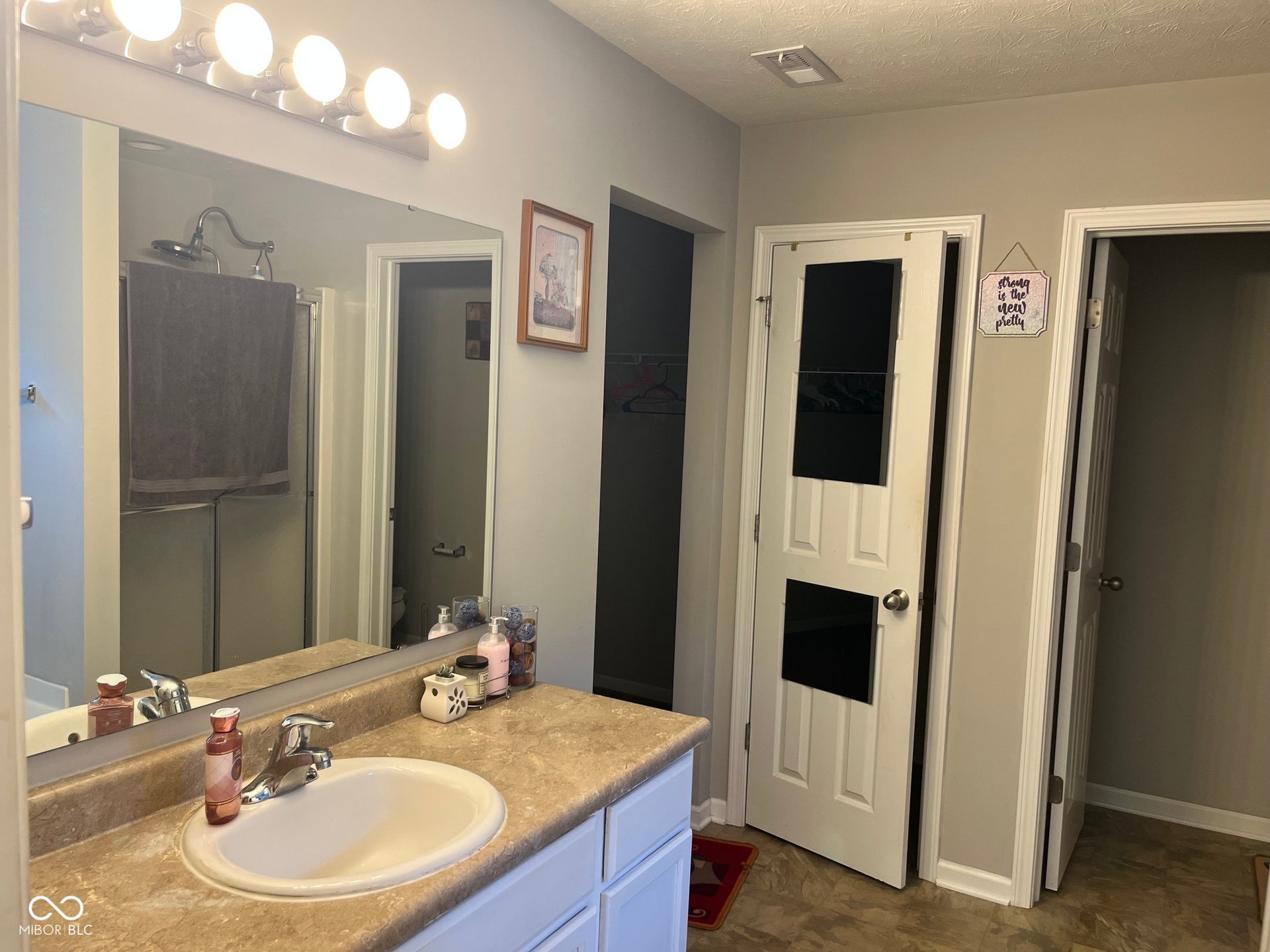 Vanity with an integrated sink and chrome faucet, large wall mirror, and a shower enclosure with a clear glass panel