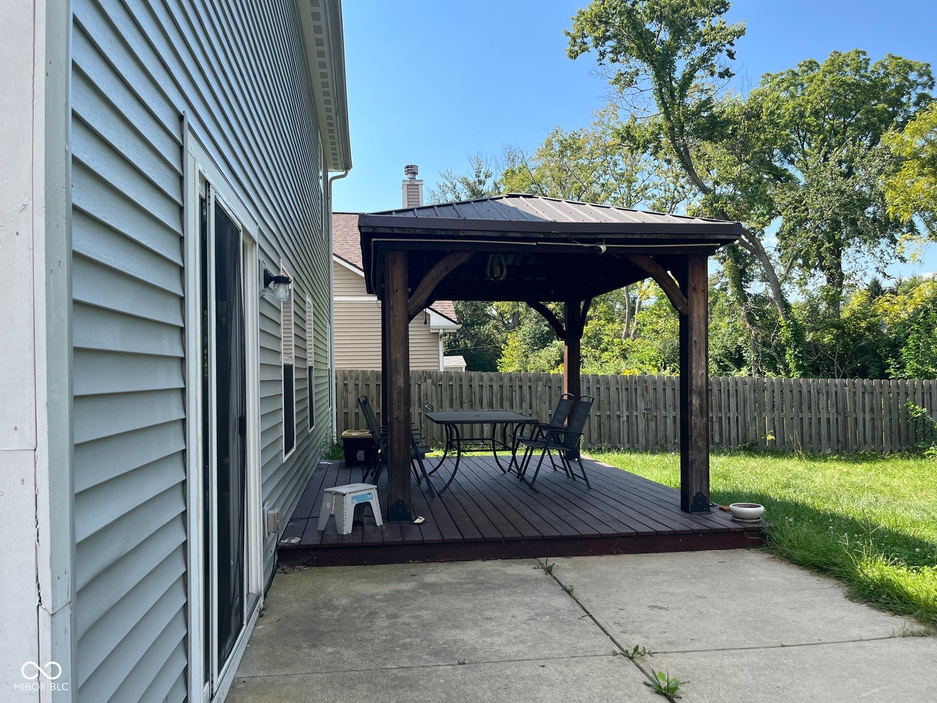 Siding exterior with a sliding glass door, leading to a wood-finish deck with a built-in gazebo and a surrounding privacy fence