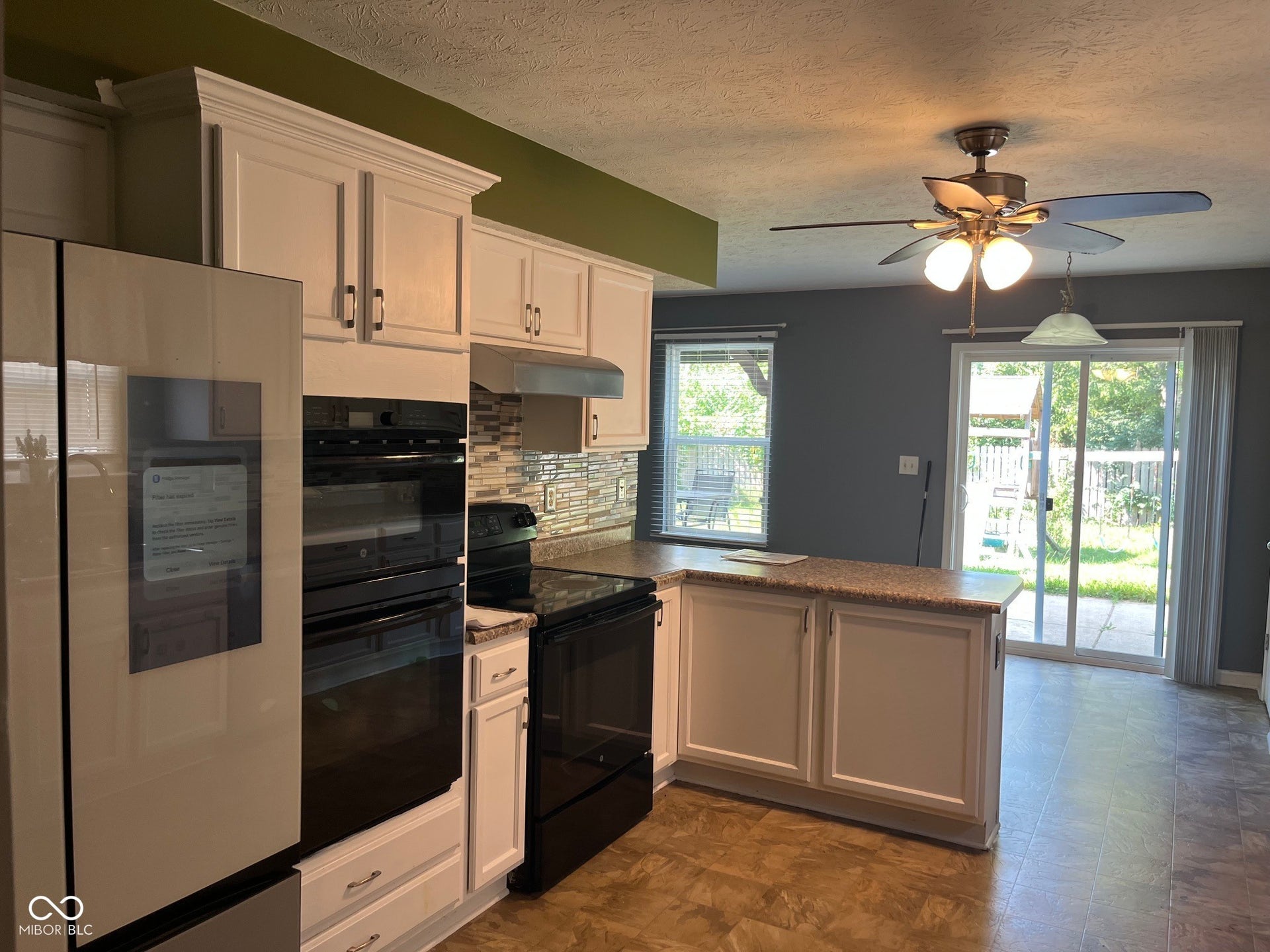White cabinetry with crown molding, integrated double wall ovens, a tile backsplash, durable wood-finish flooring, and a sliding glass door to the exterior