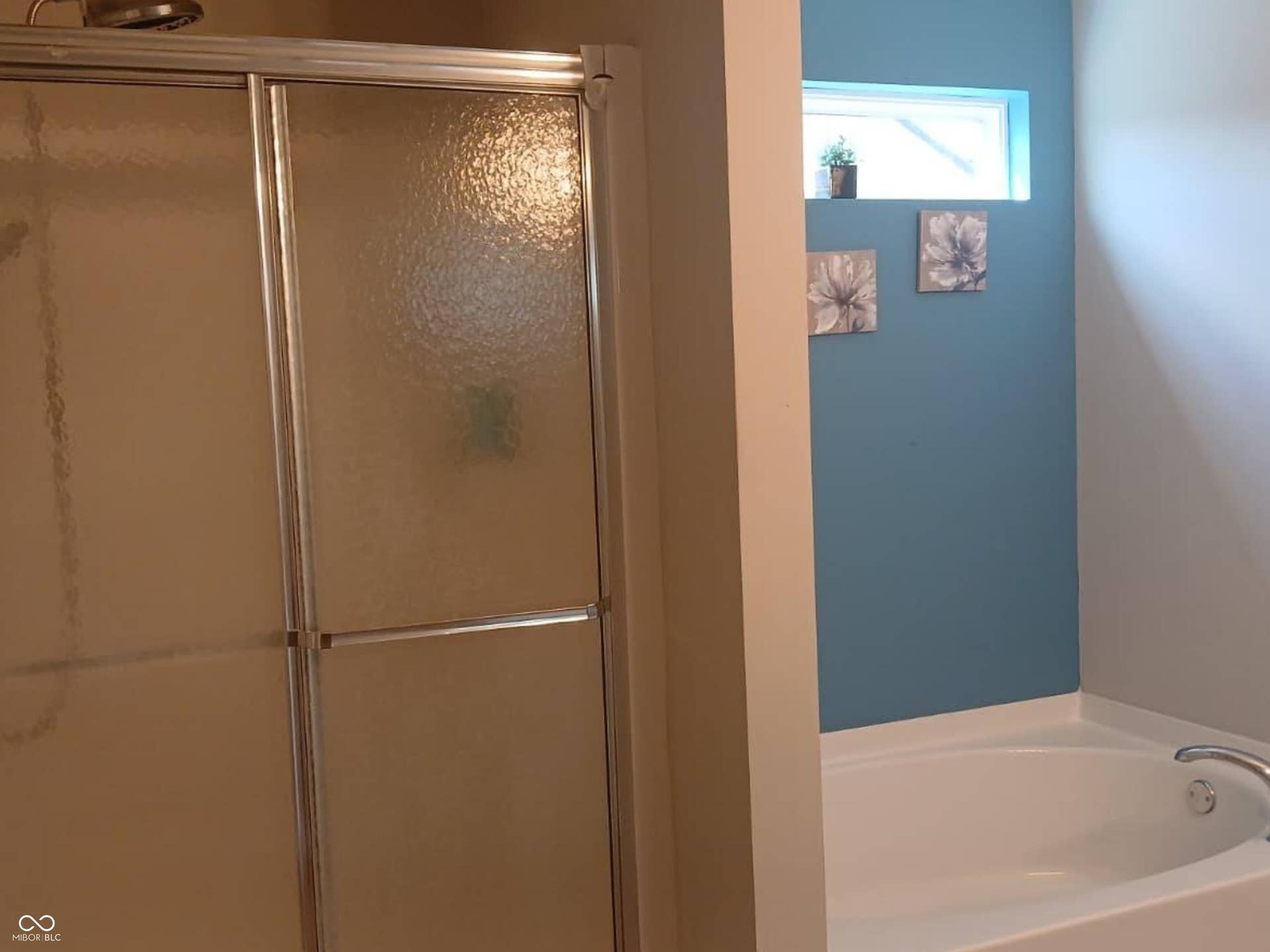 Built-in soaking tub with chrome fixtures, an adjacent shower with sliding frosted glass doors, and a decorative wall niche