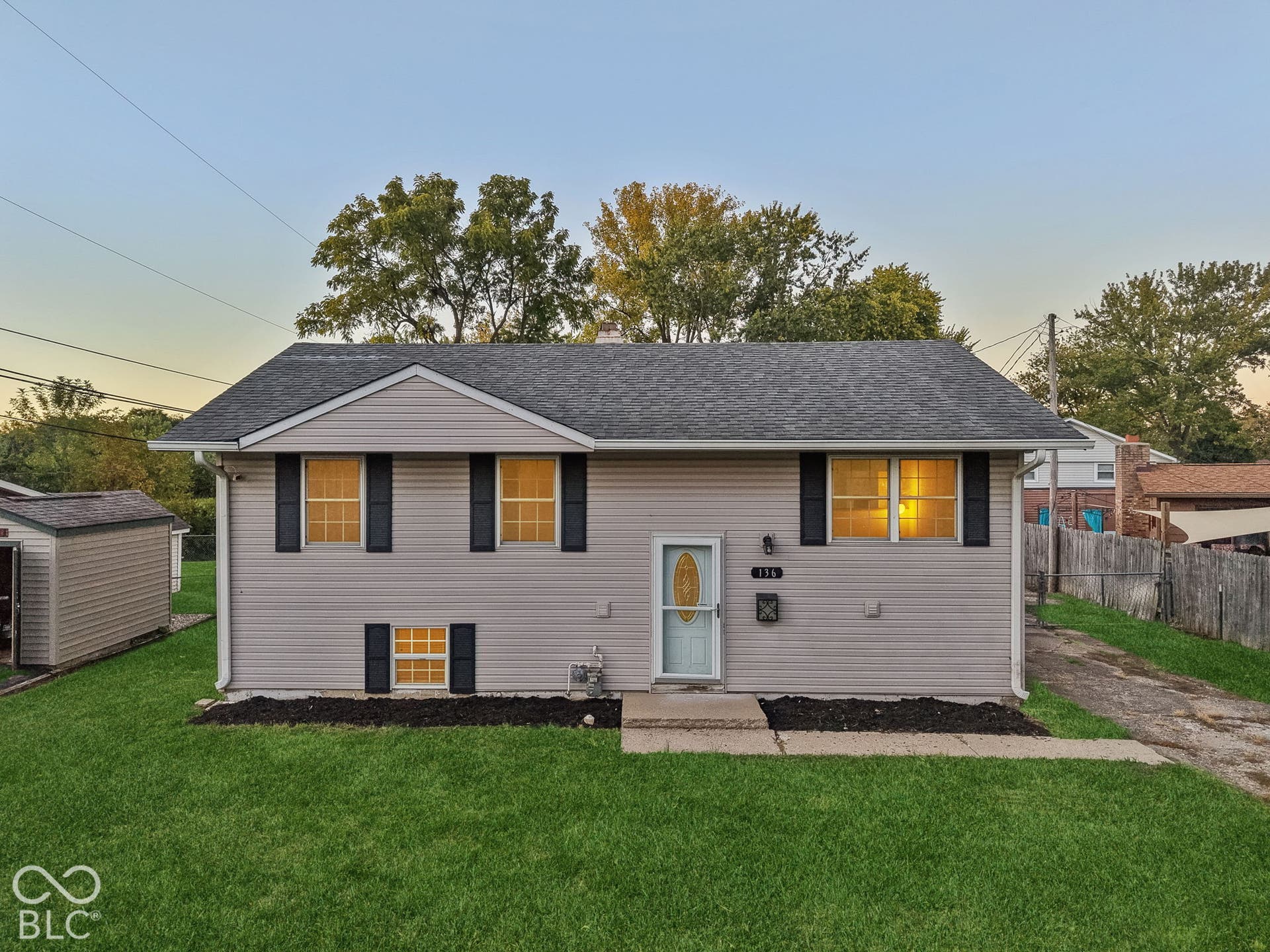 Virtually Altered - Light-colored siding exterior with a dark shingle roof, black window shutters, and a front entry door with an oval glass insert