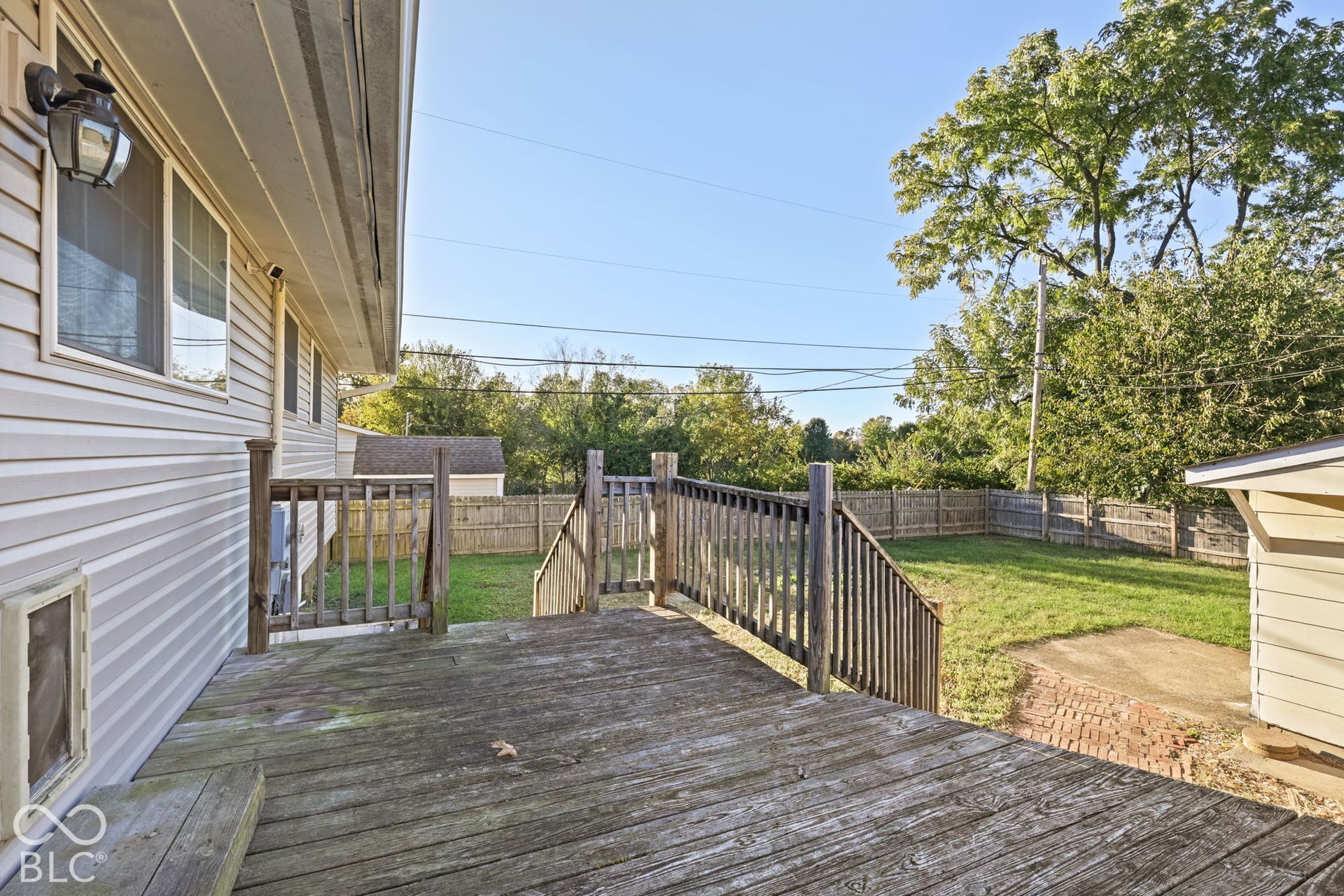 Exterior deck with wood railings, overlooking a fenced backyard with a grass lawn