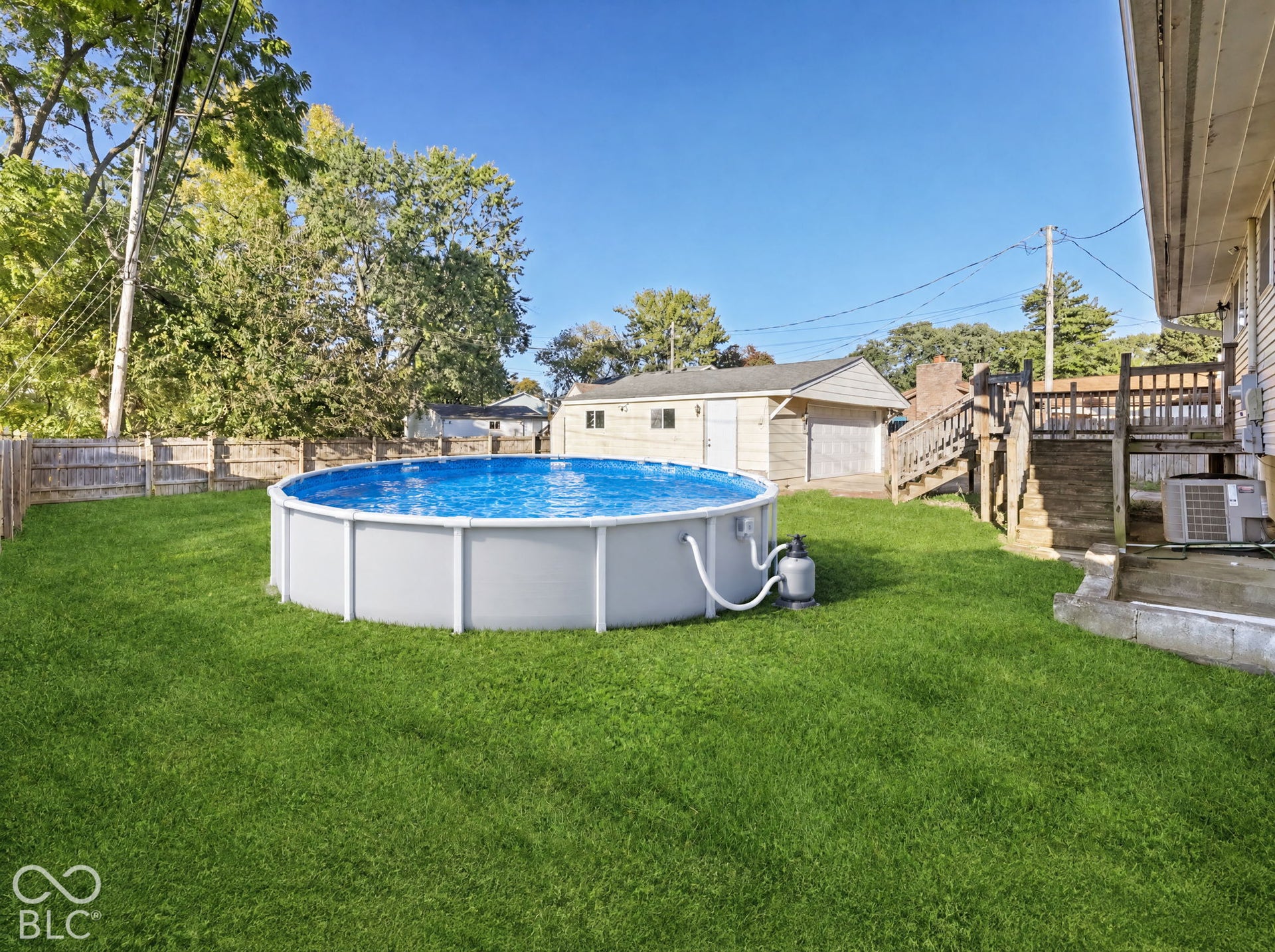 Virtually Altered - Expansive rear yard featuring an above-ground pool, a wooden privacy fence, a detached garage, and a raised wood deck with railing